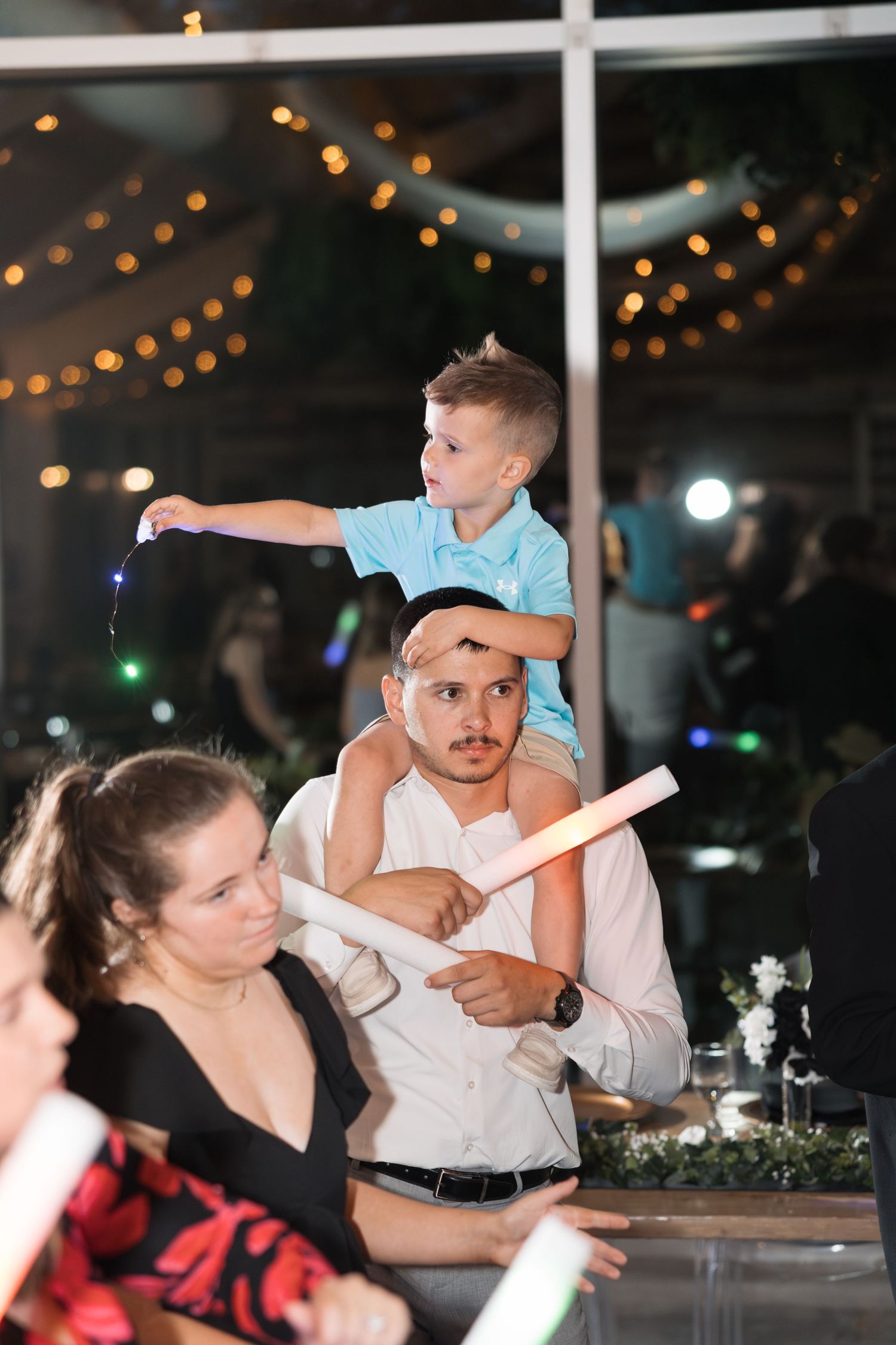 A young child sits on someone's shoulders during a wedding reception celebration.