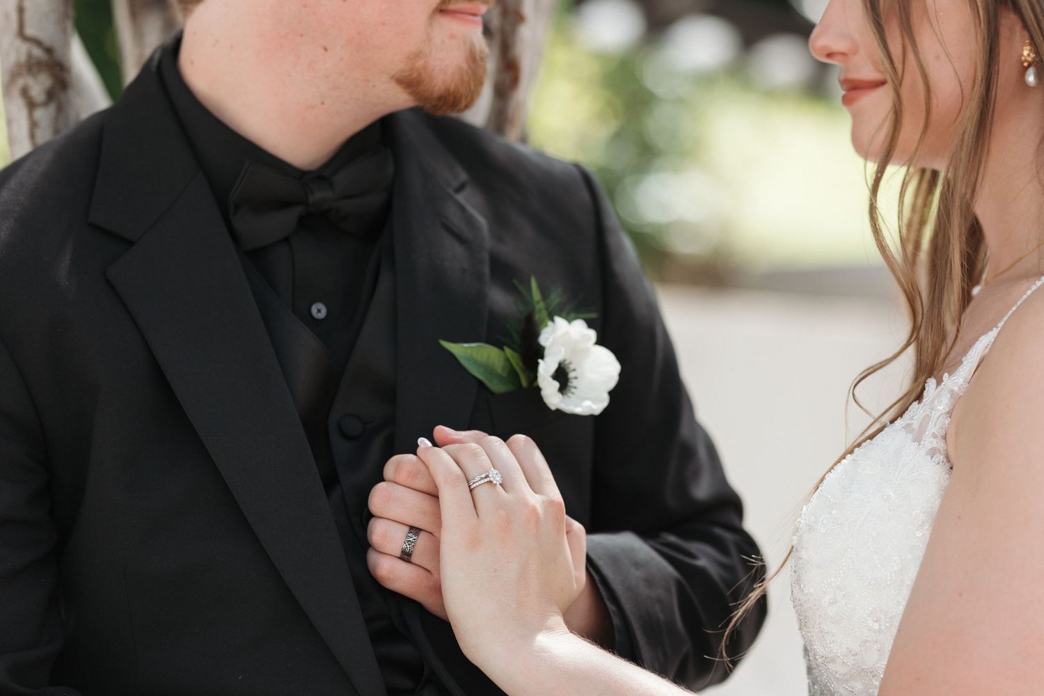 Close-up of newlyweds holding hands showing white boutonniere detail.