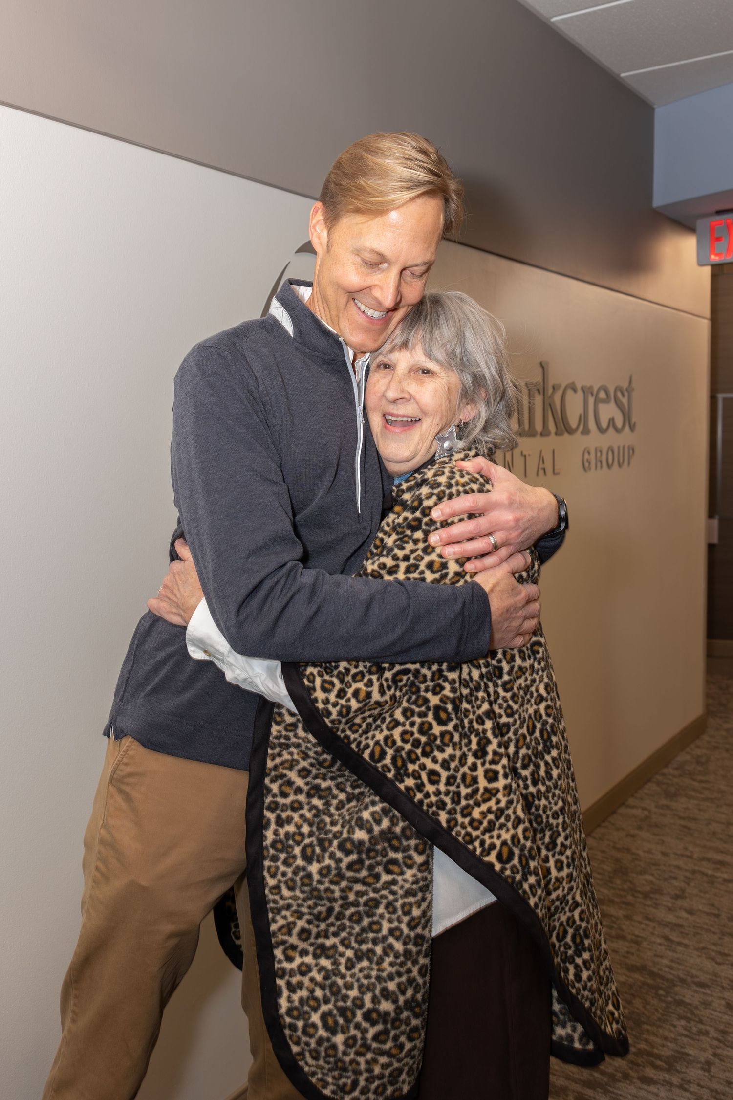 Two people share a warm embrace in an office hallway with Parkcrest signage visible.