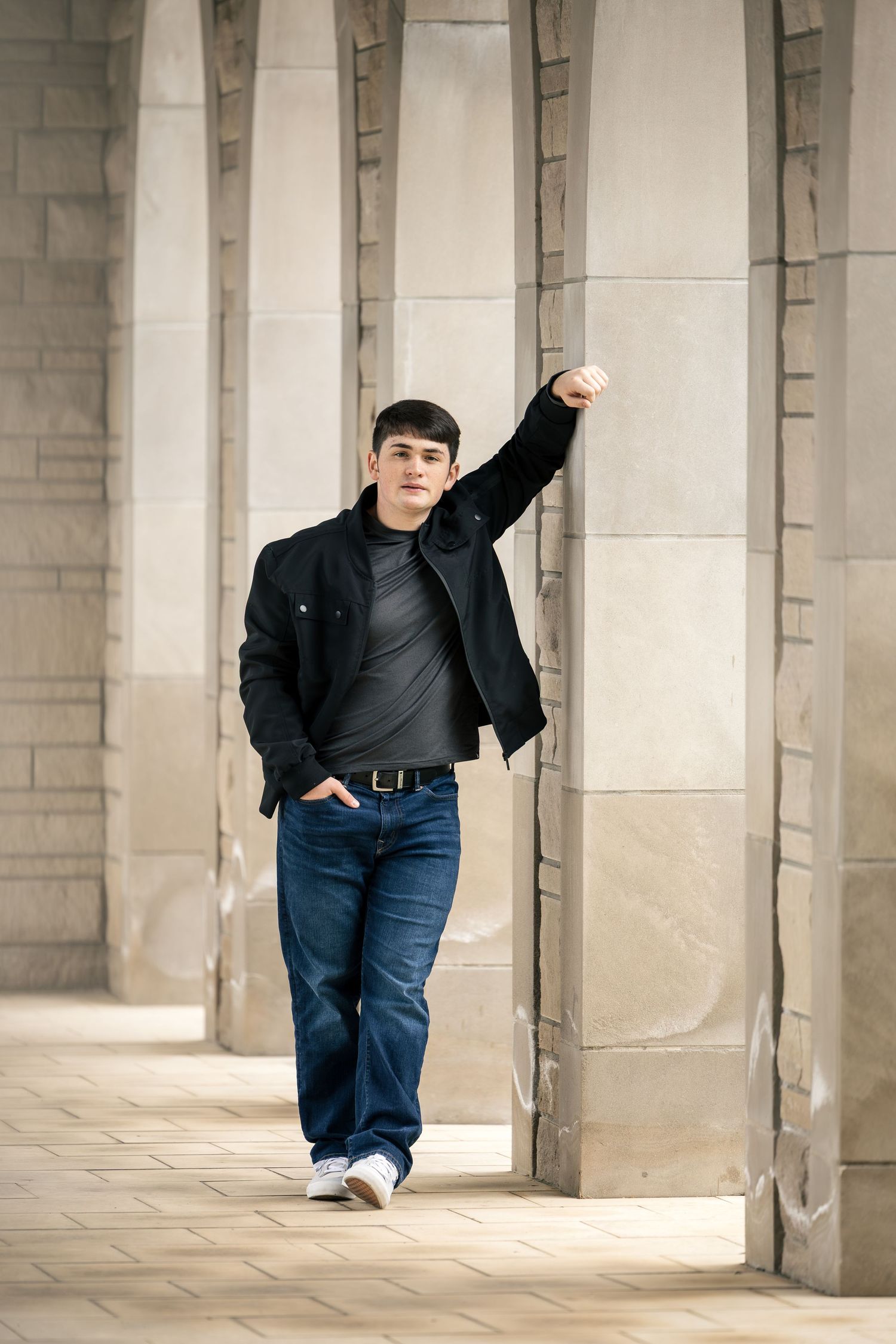 A person poses between stone pillars in a long colonnade walkway.