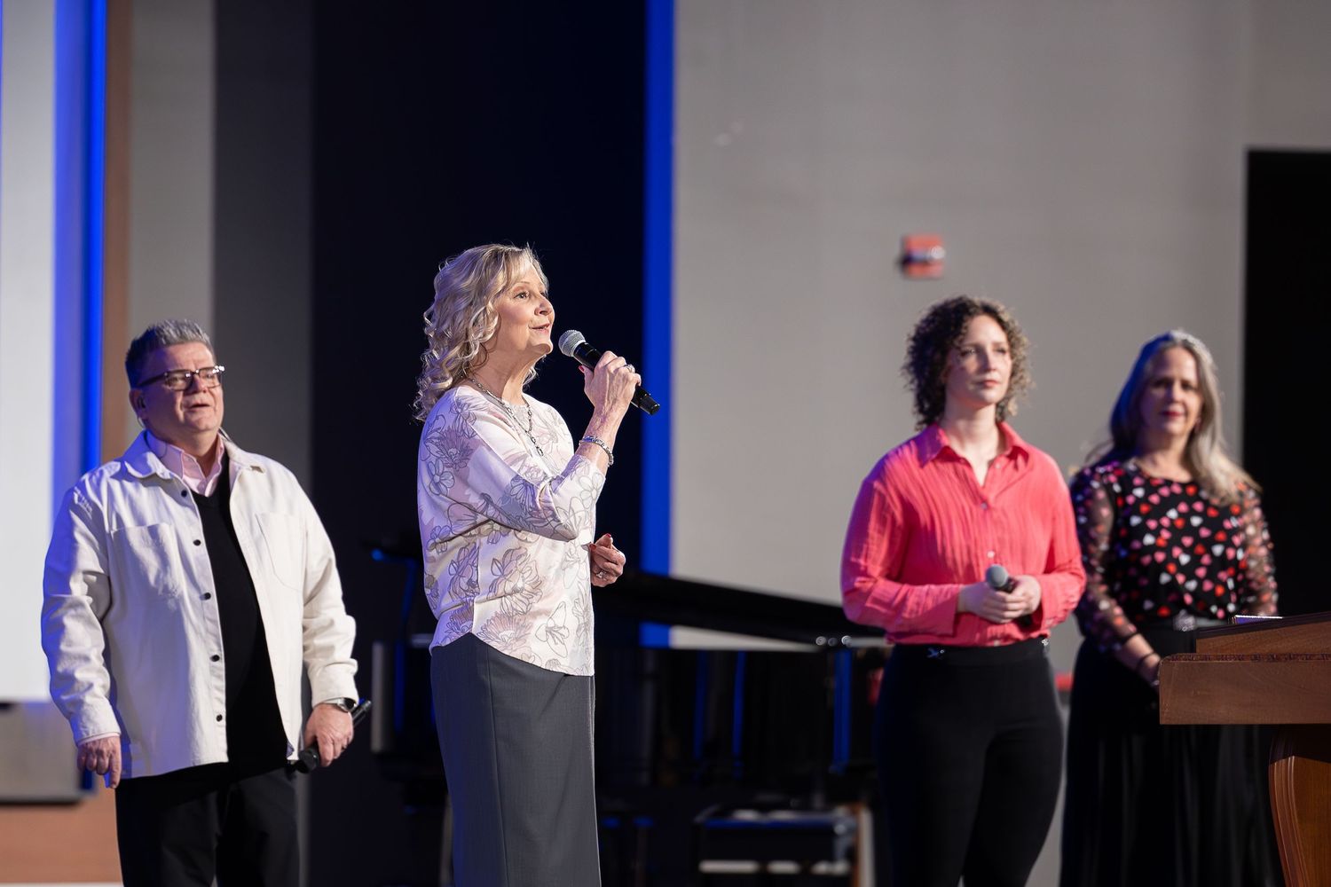 Worship team performs on stage during a church service with blue accent lighting.