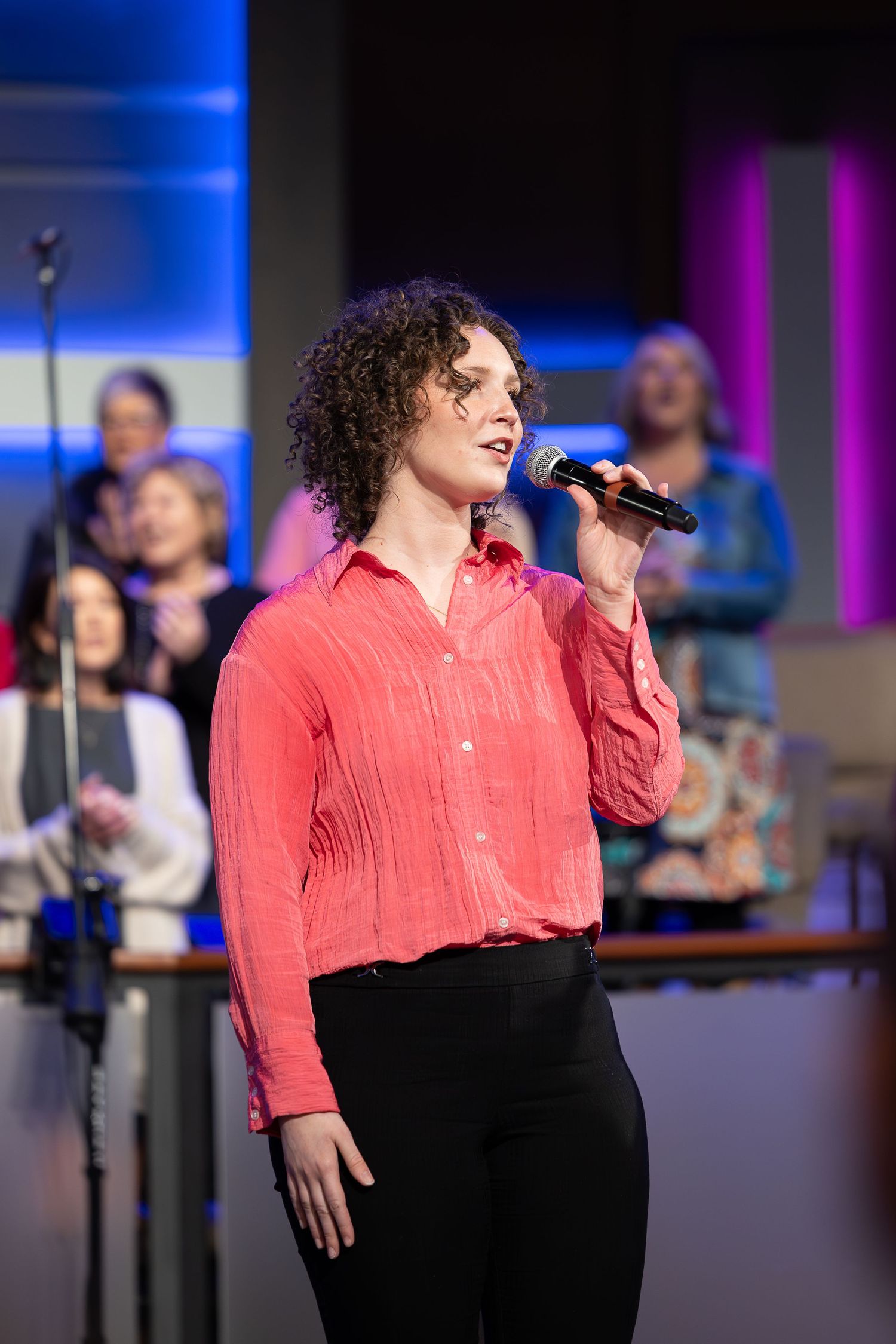 Singer performs in a coral red shirt against blue stage lighting during a musical performance.