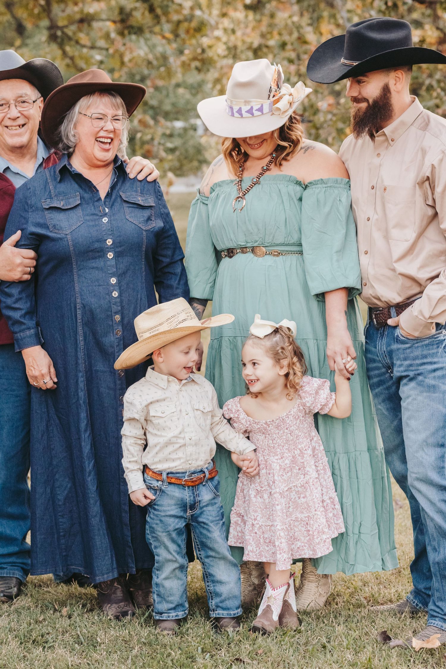 Family group in western wear poses outdoors with young children in matching country attire.