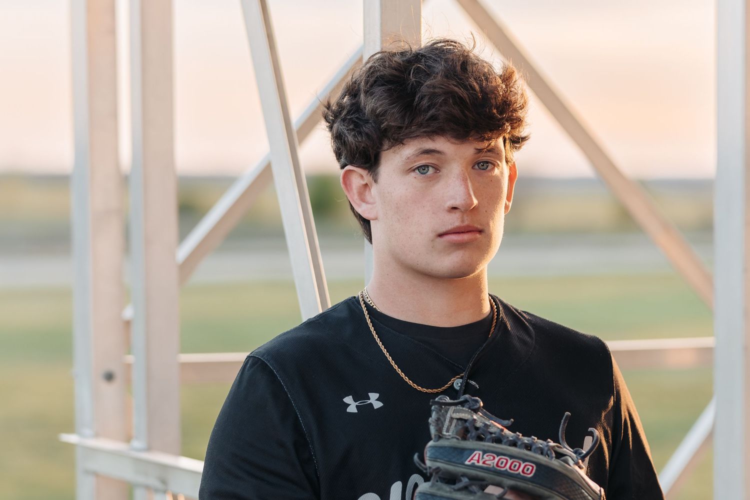 Athletic figure in black Under Armour shirt posed against metal structure at sunset.