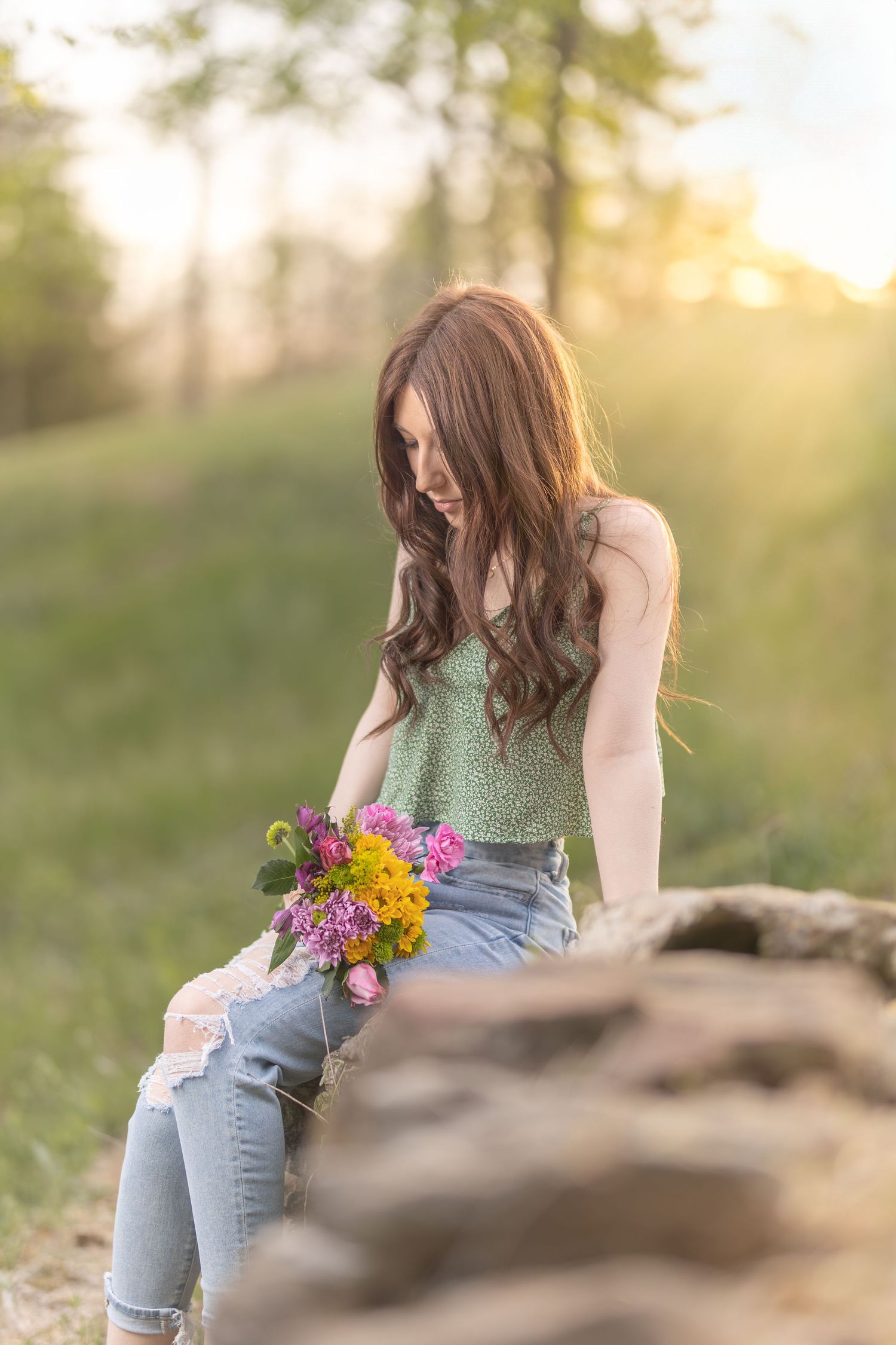 A casual portrait with colorful wildflower bouquet sitting on rocks in evening sunlight.
