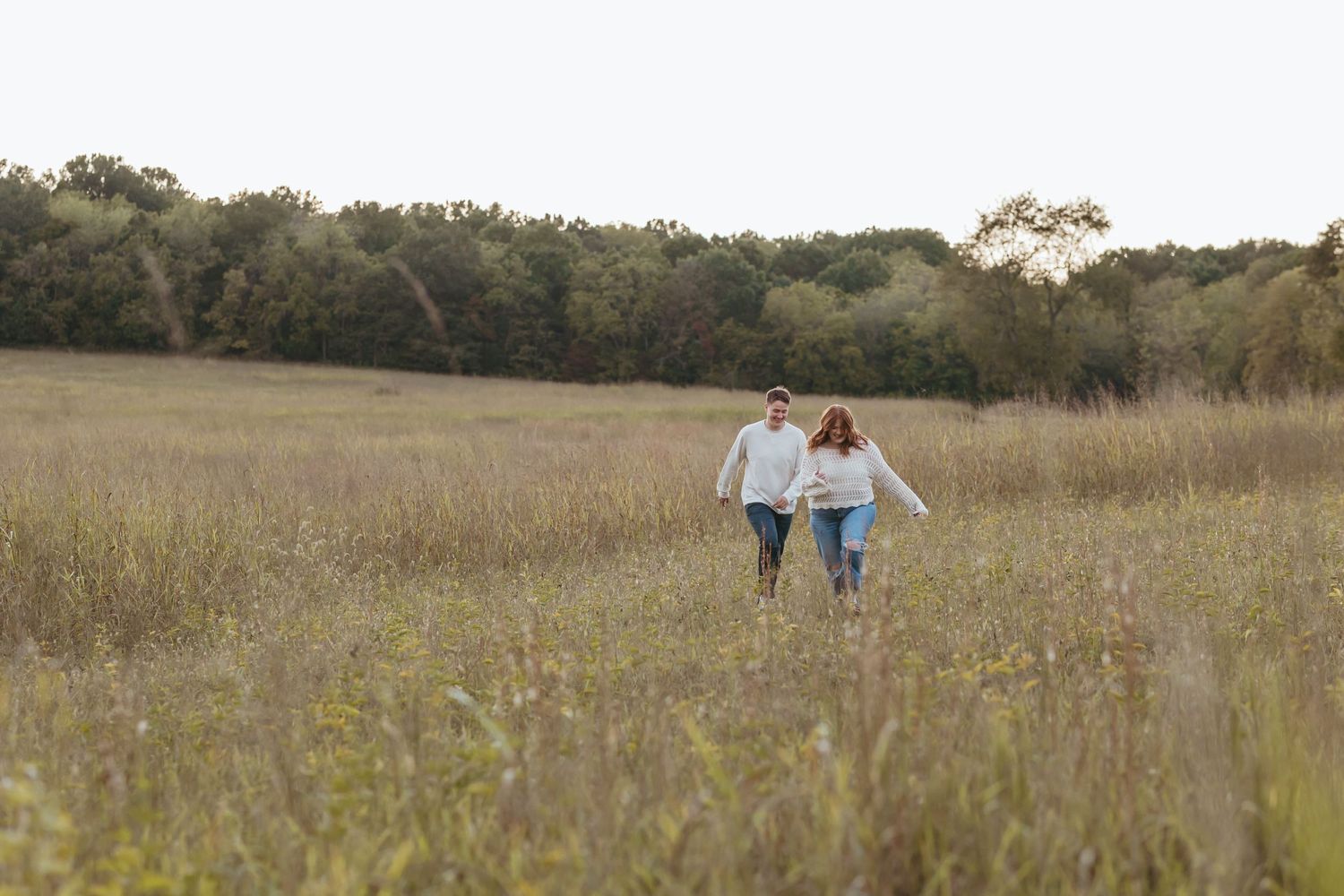 Couple enjoying a romantic walk through a sunlit meadow with trees in background.