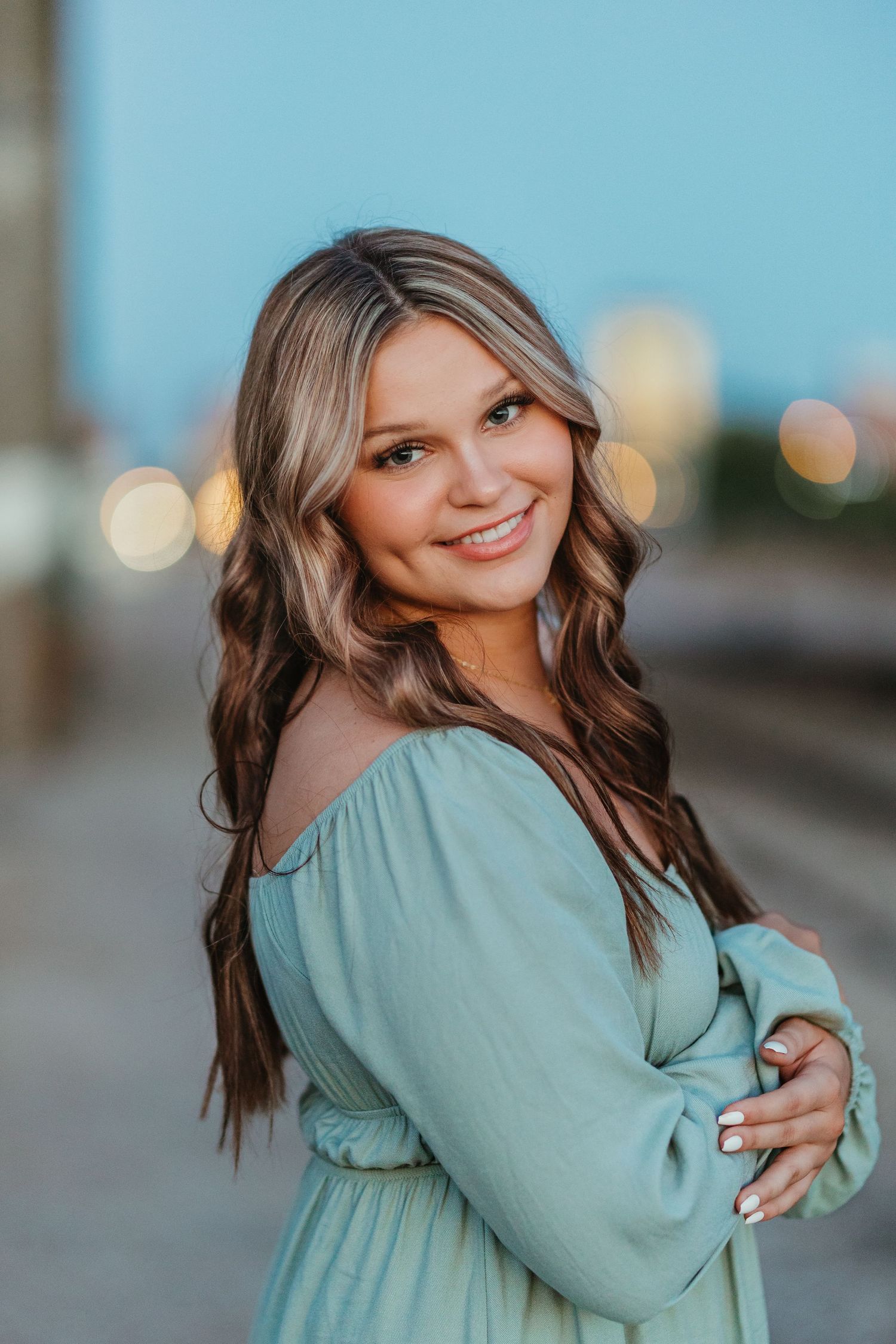 A lifestyle portrait of someone in a turquoise off-shoulder dress against an urban background.