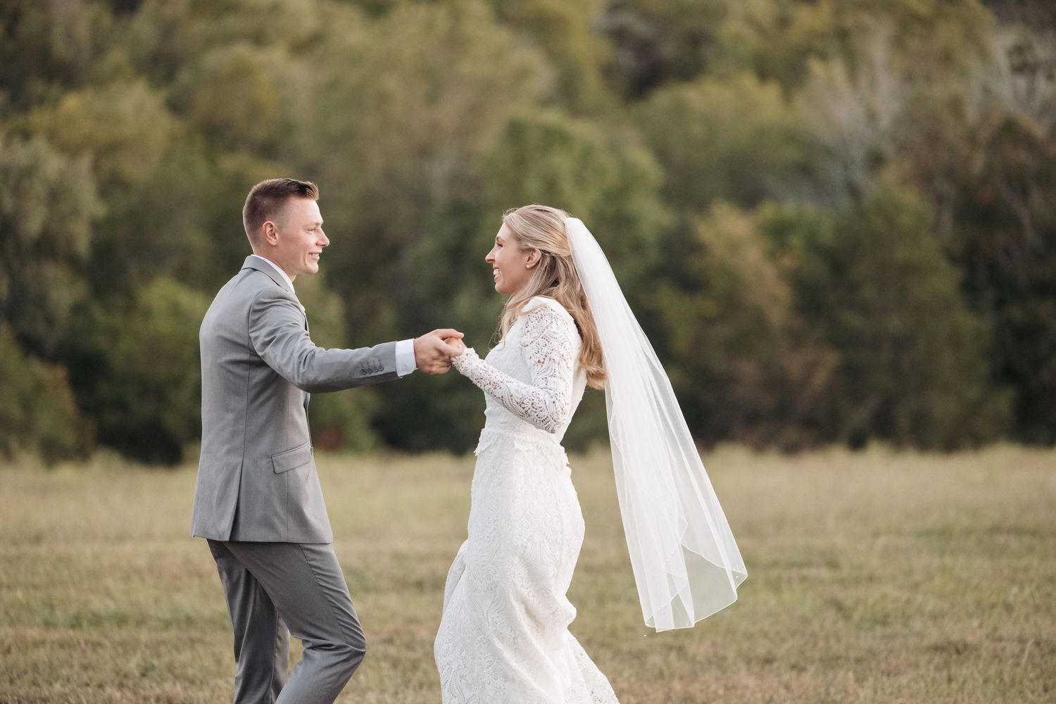 Wedding couple dances playfully in an open field with mountains in background.