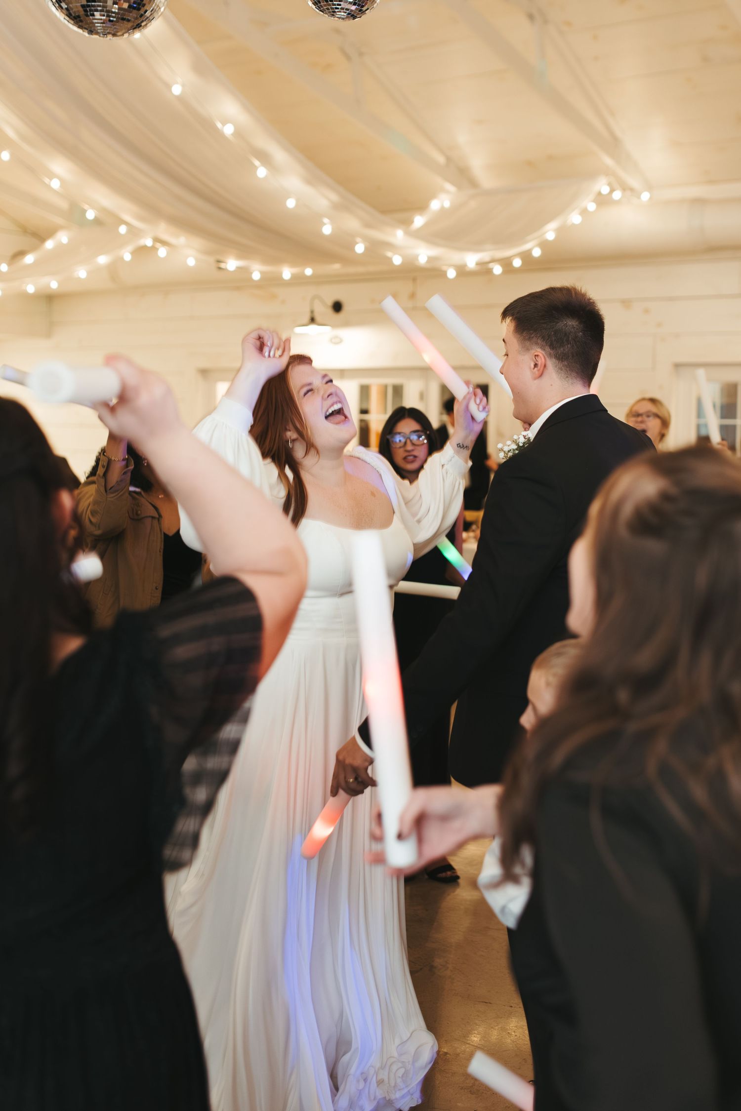 Celebration on dance floor with bride in flowing white dress surrounded by dancing guests.