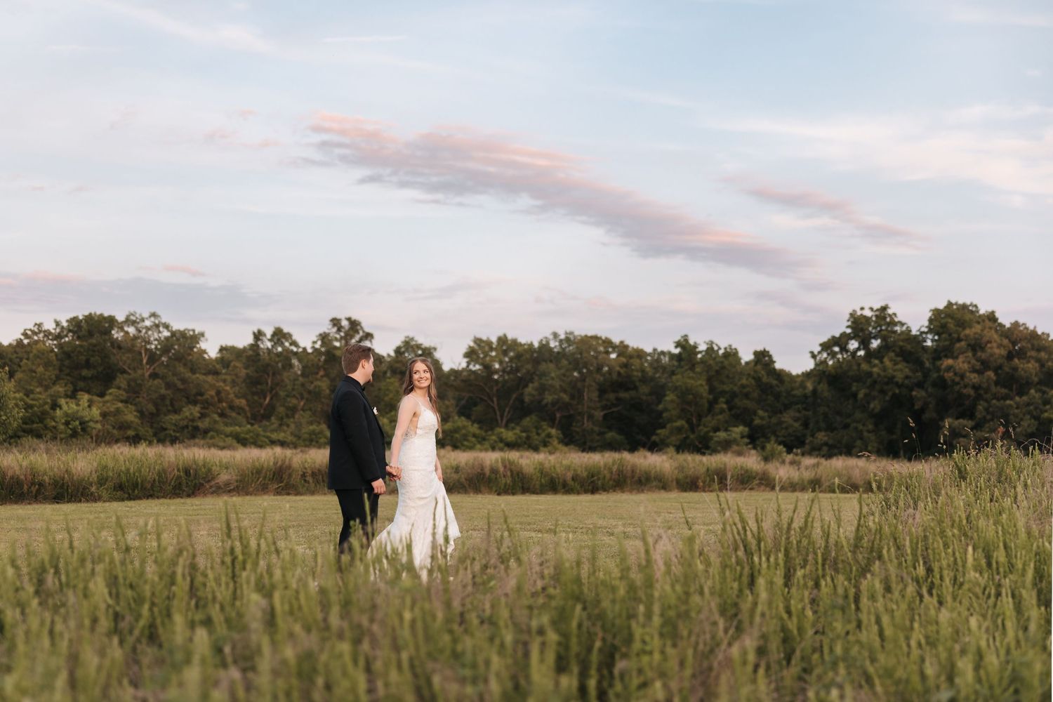 A bride and groom share a quiet moment together in a tall grass field at dusk.