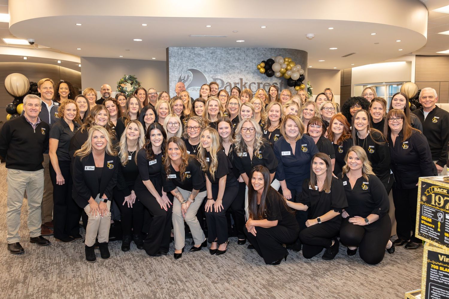 Large group of employees in navy and black attire pose together for corporate photo.