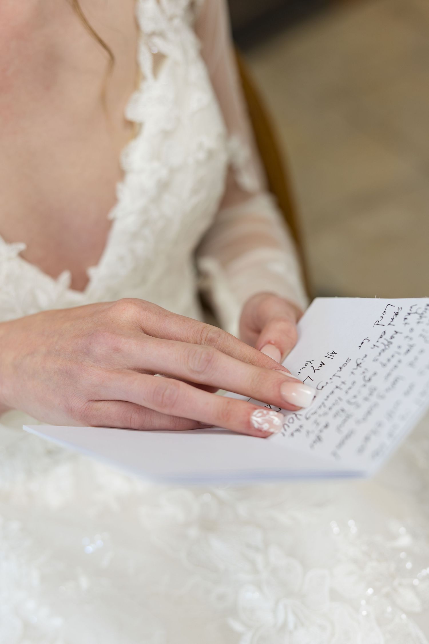 Bride in lace wedding dress reads handwritten letter with manicured nails on wedding day.