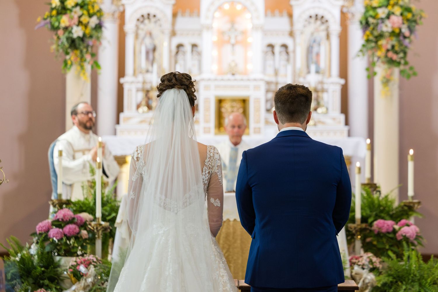 Bride and groom stand at the altar of a beautifully decorated Catholic church during their wedding ceremony.