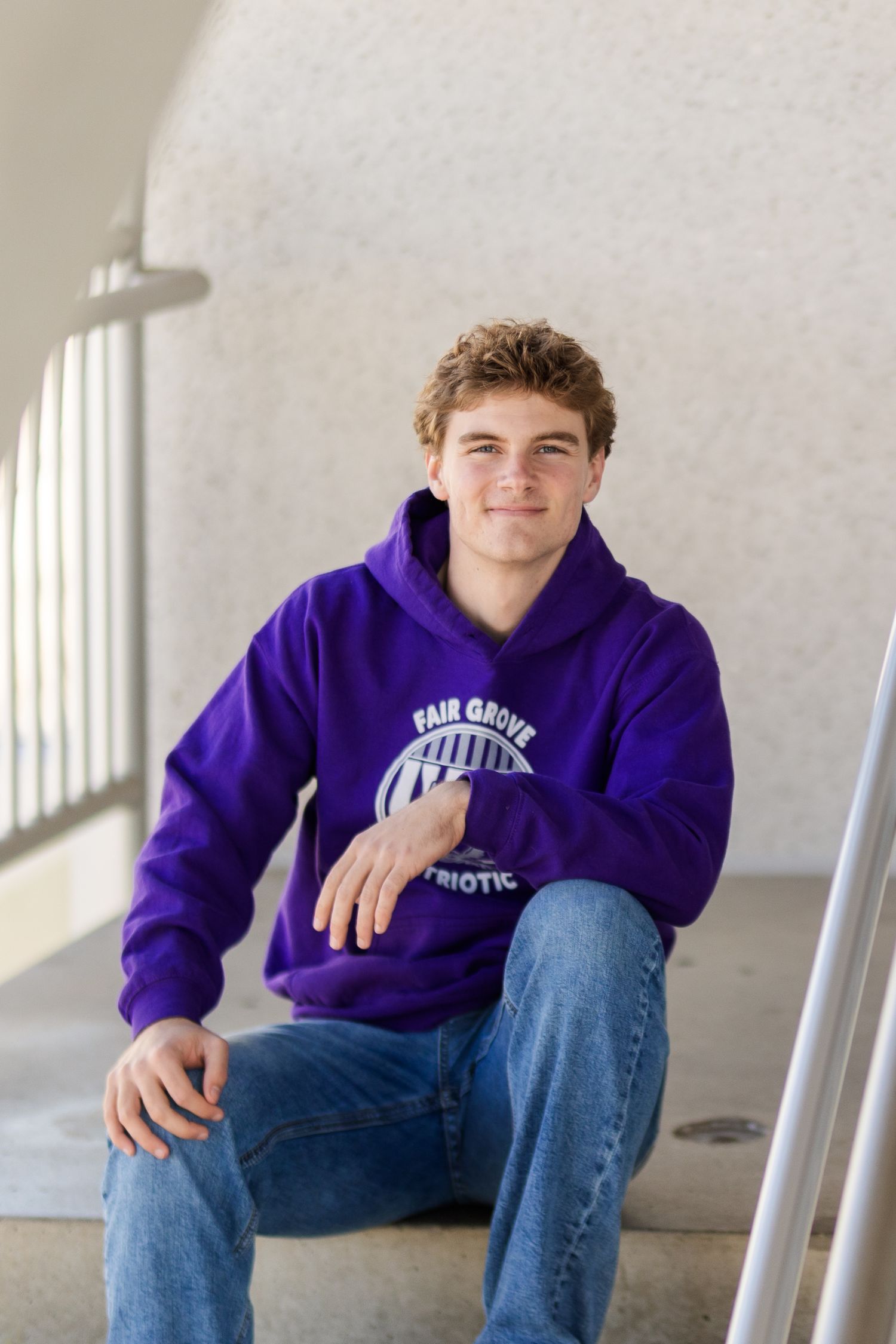Student wearing purple sweatshirt and jeans sitting casually on steps with white pillars in background.