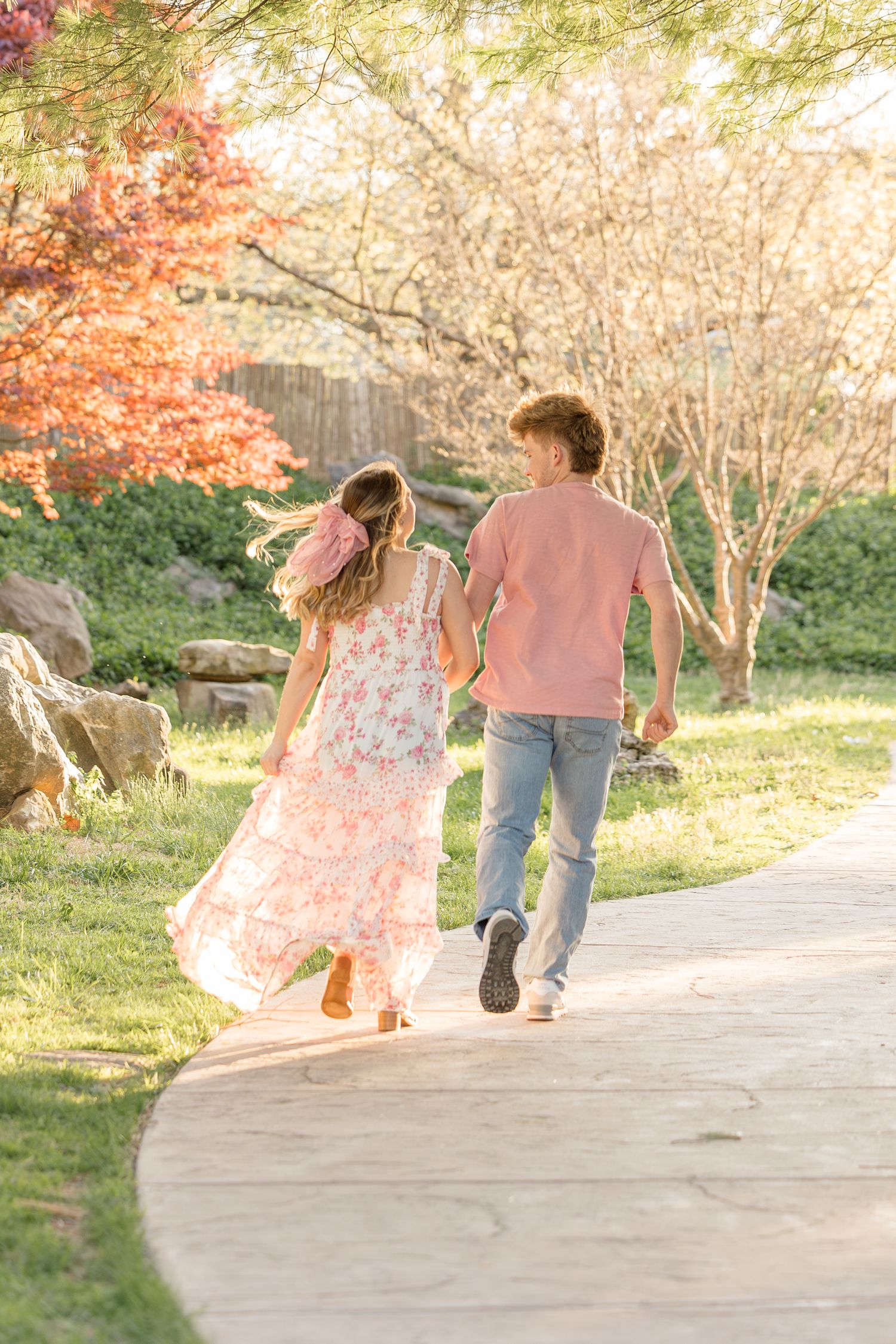 A couple walks hand in hand down a garden path surrounded by autumn foliage and blossoming trees.