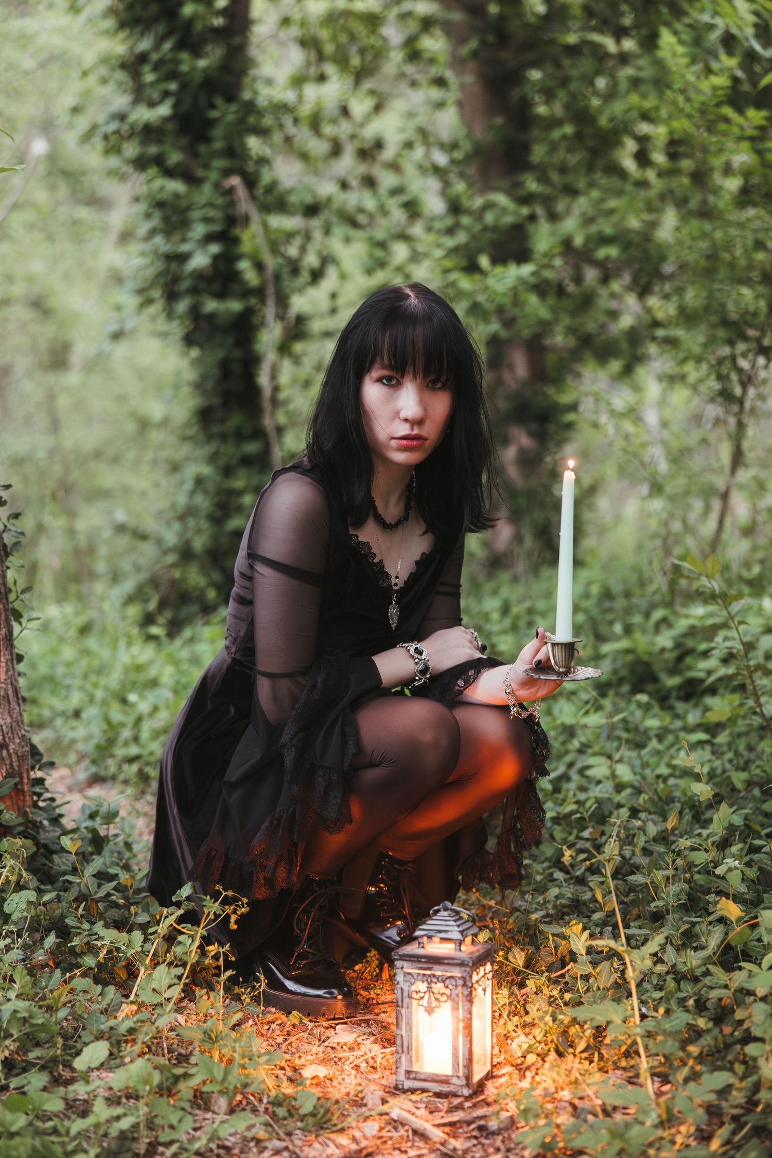 A gothic-styled scene in a forest with a lantern glowing among fallen leaves and dark clothing.