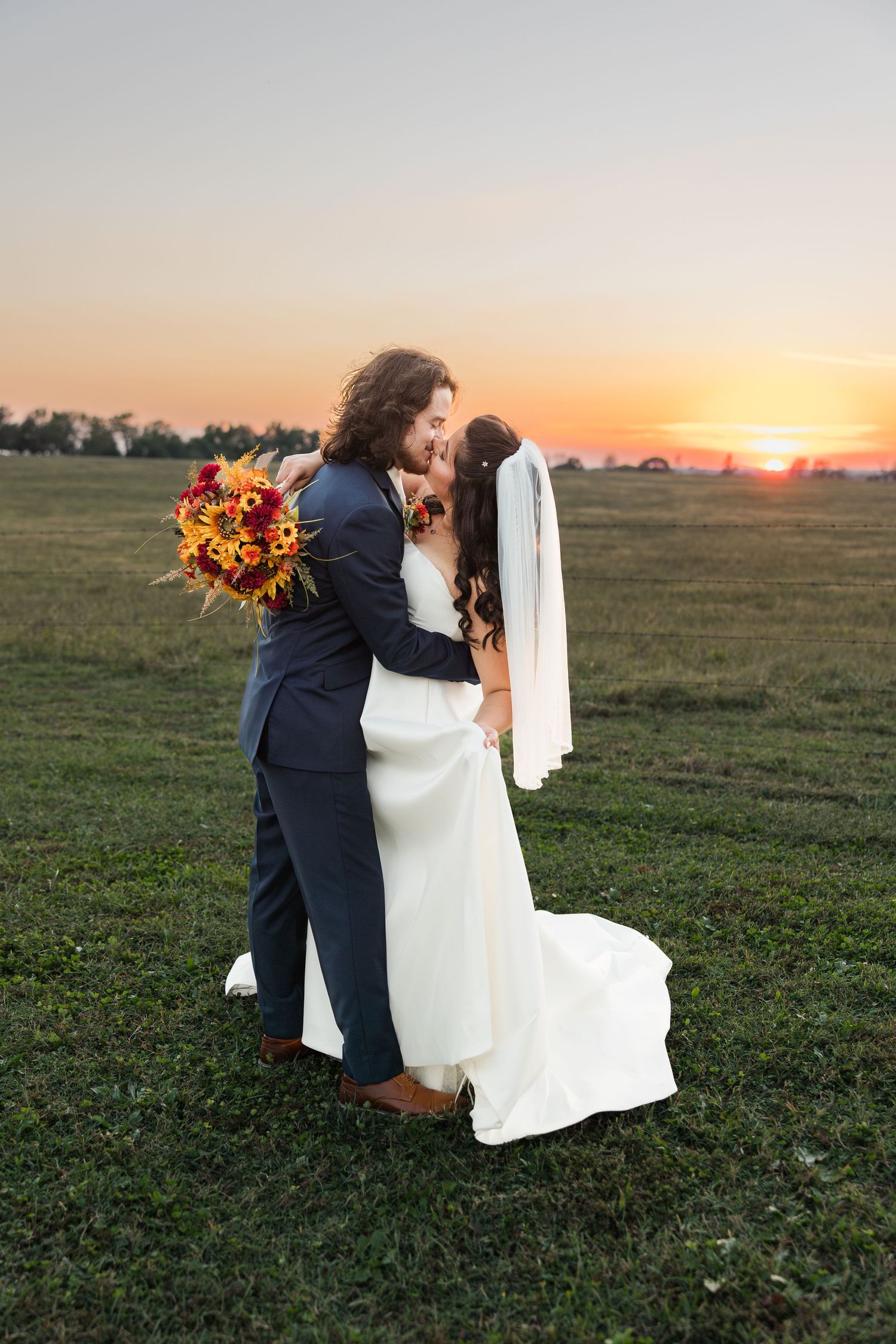 Newlyweds share an intimate moment in a field at sunset with golden light and fall colors.
