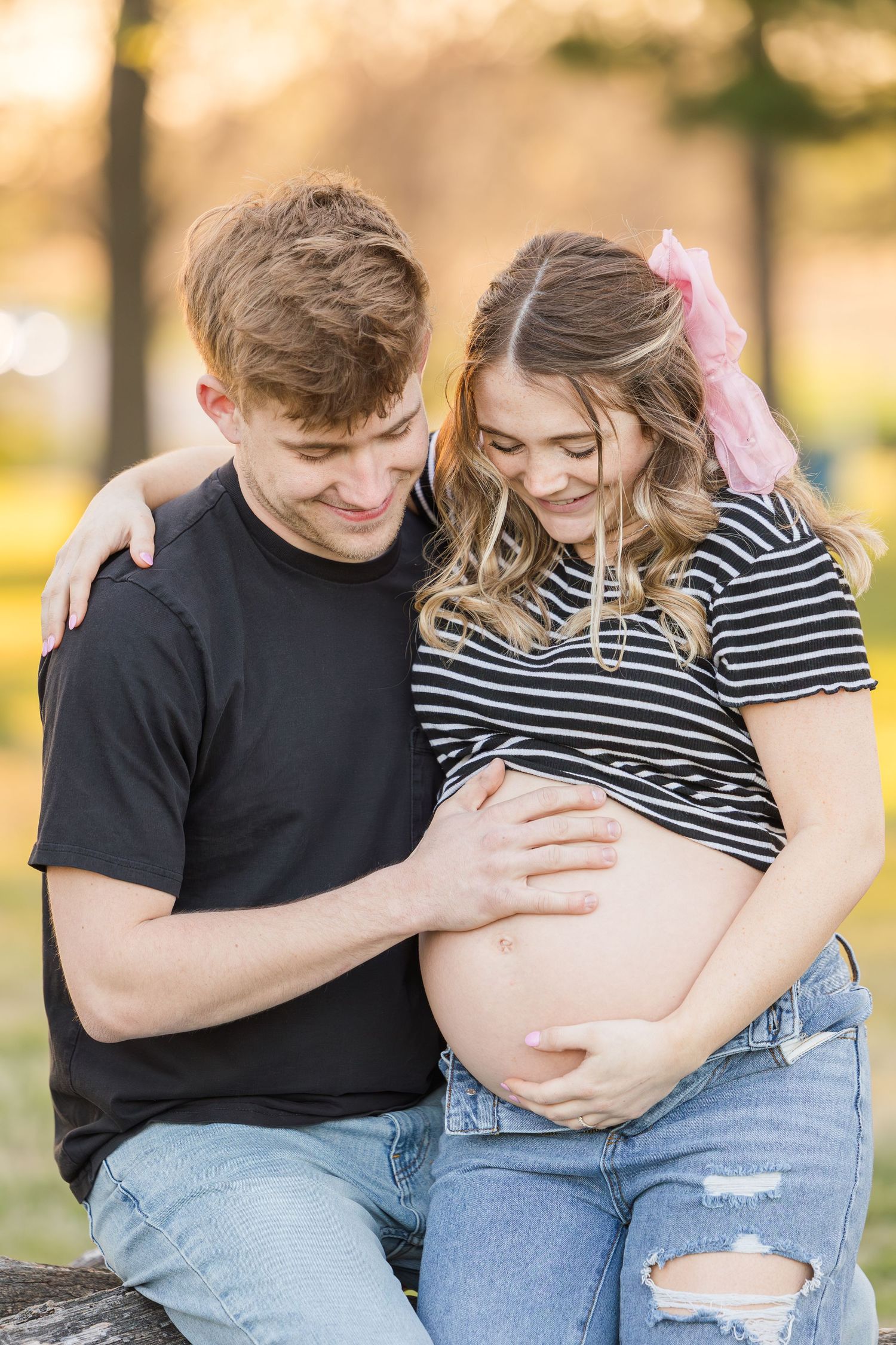 An expectant couple shares a tender moment outdoors in autumn light.
