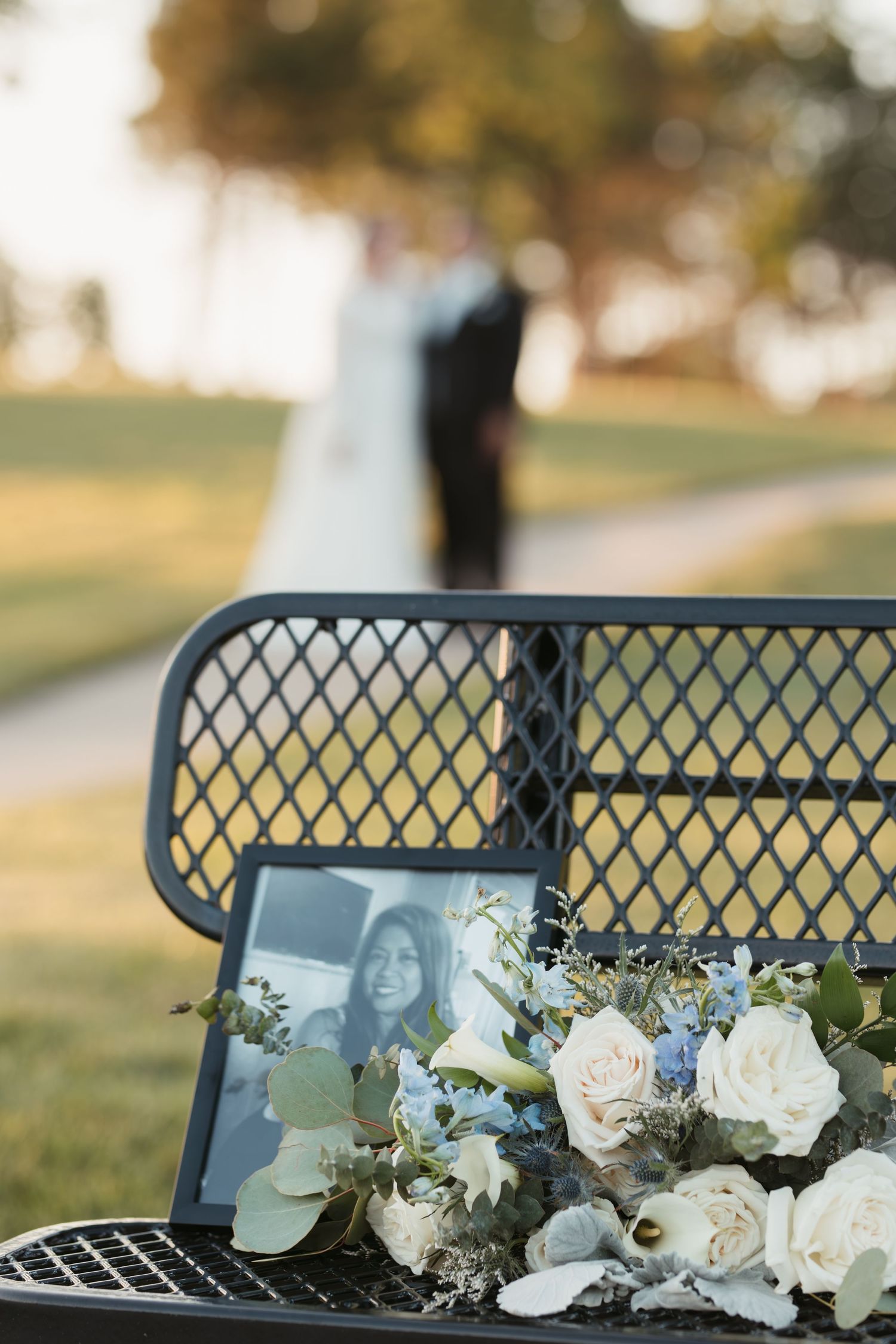 Wedding bouquet with white roses and tablet rests on metal bench during outdoor photography session.