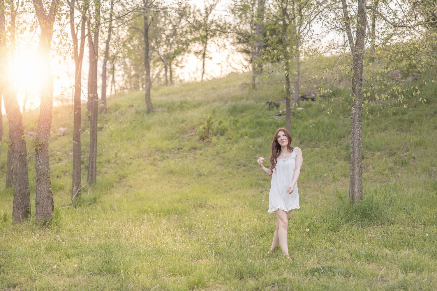 A serene photo of someone in a white dress walking through a sunlit forest.