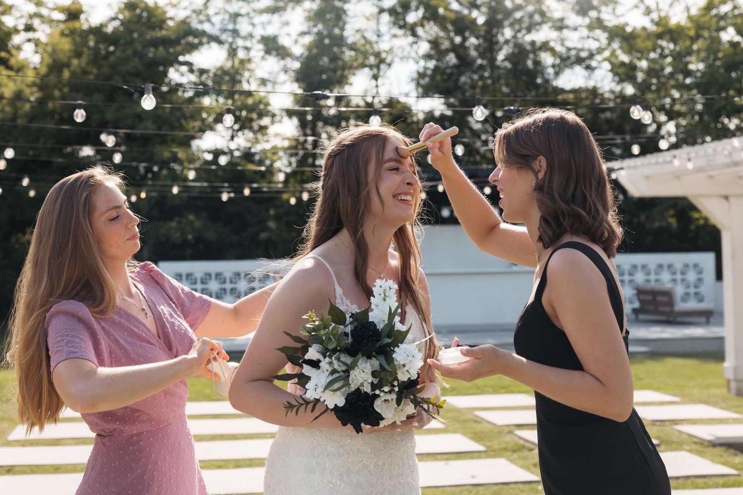 Three friends share joyful moment with bouquet during outdoor wedding celebration.