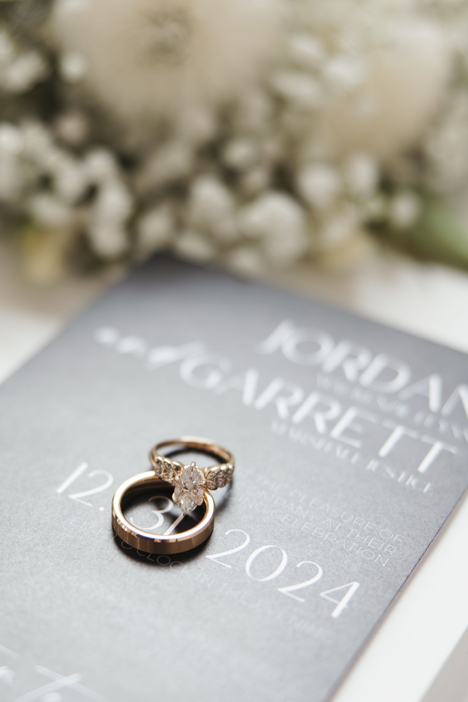 Wedding rings placed on grey wedding invitation with date December 2024.