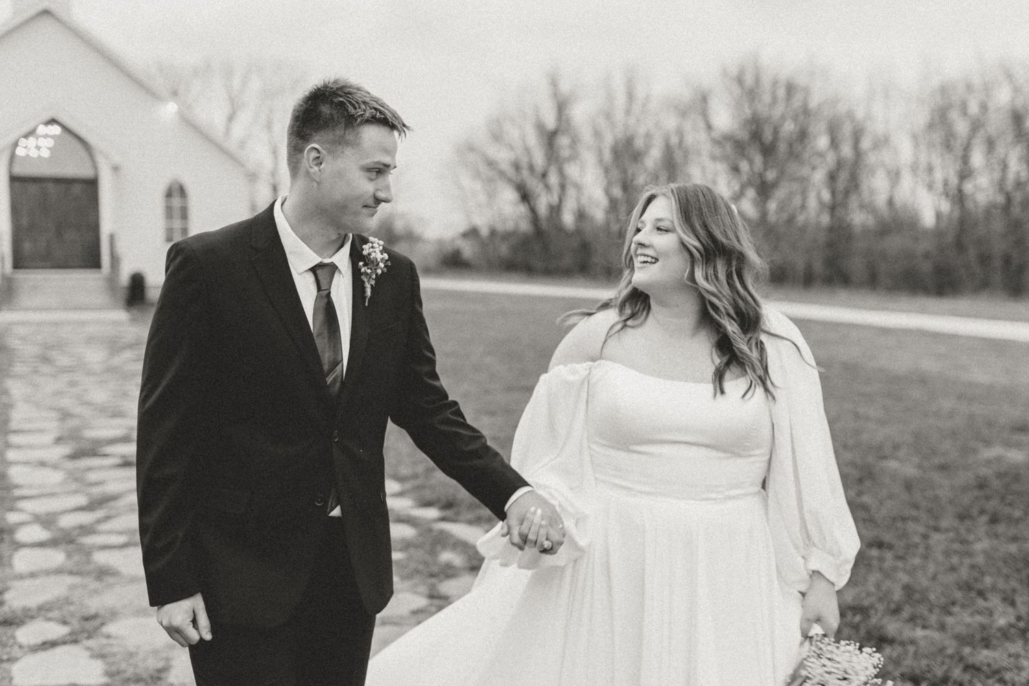 Newlyweds share a joyful moment walking together outside a white chapel.