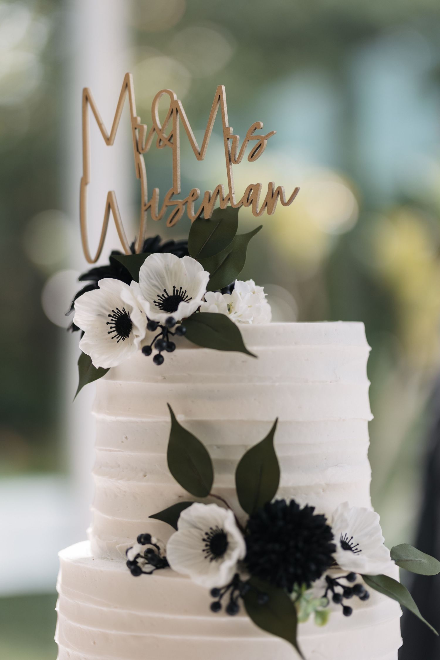 Elegant white wedding cake decorated with black and white flowers and a gold Mr & Mrs topper.