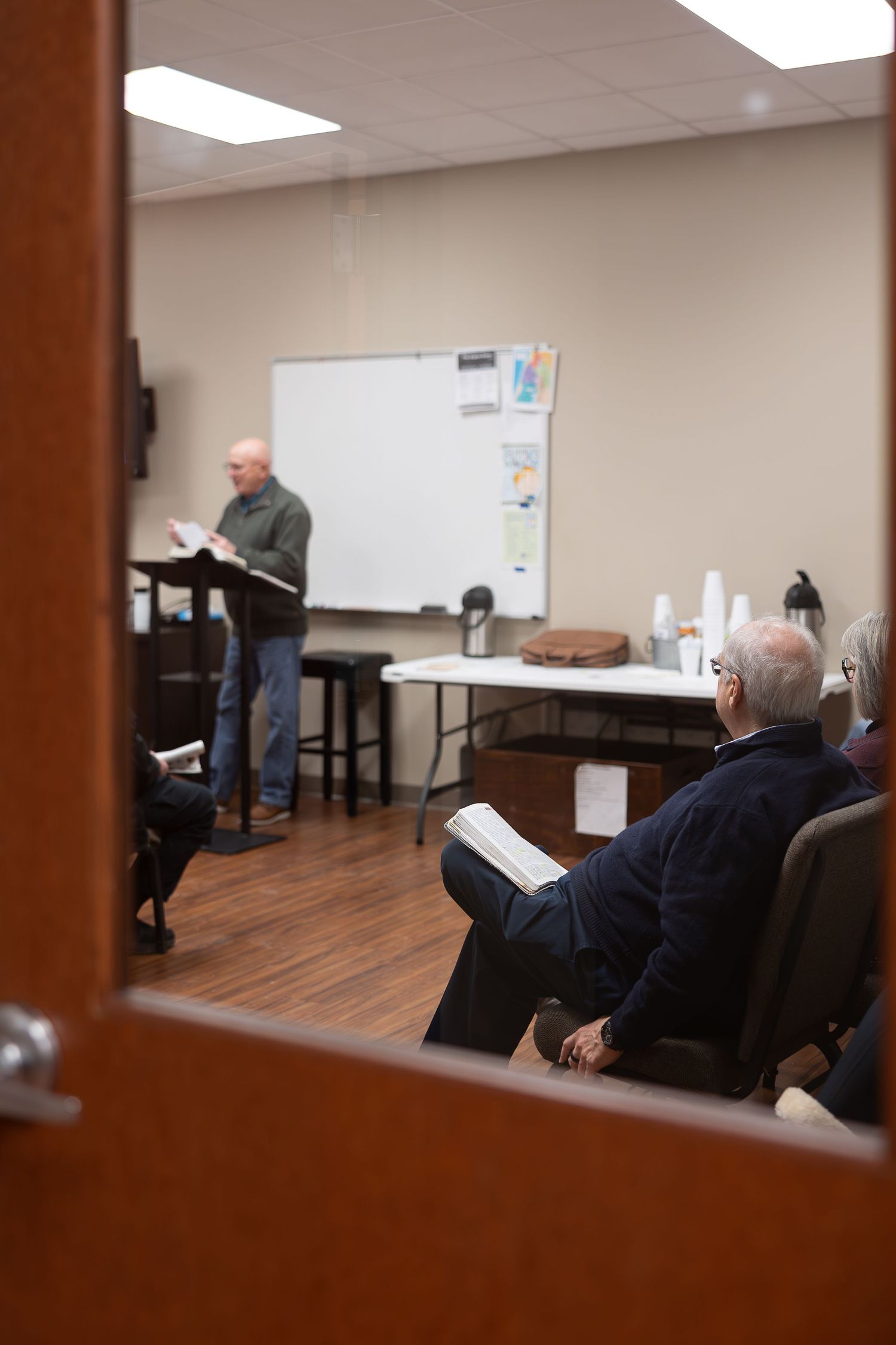 Classroom setting viewed through doorway with people reviewing materials.