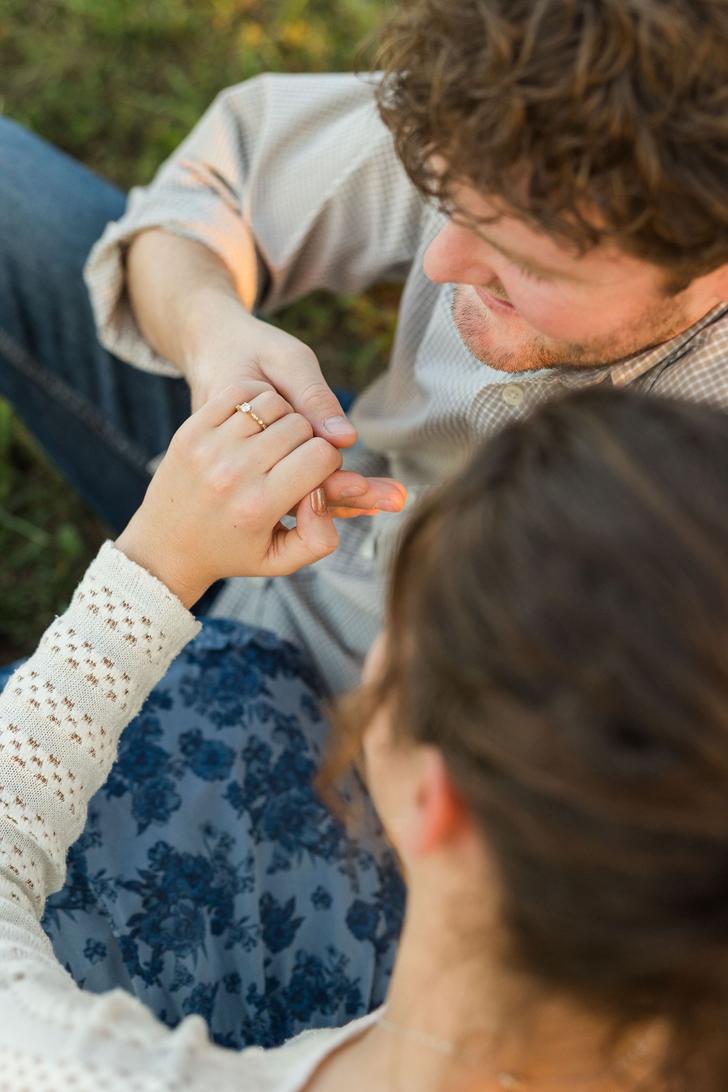 An intimate moment captured as a ring is placed on a hand during an outdoor proposal.