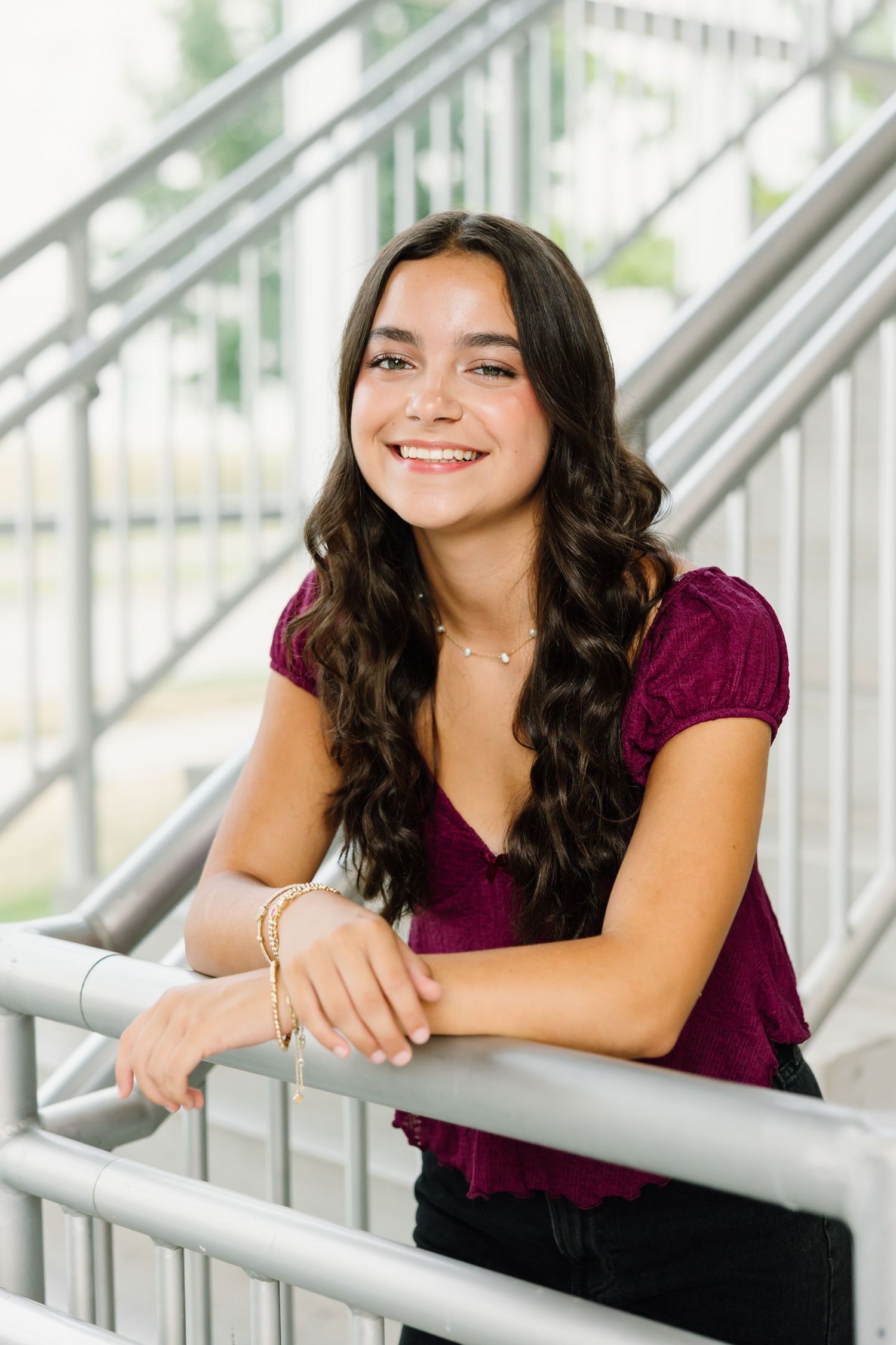 Person wearing a burgundy top leans on a metal railing in a bright modern building interior with natural lighting.