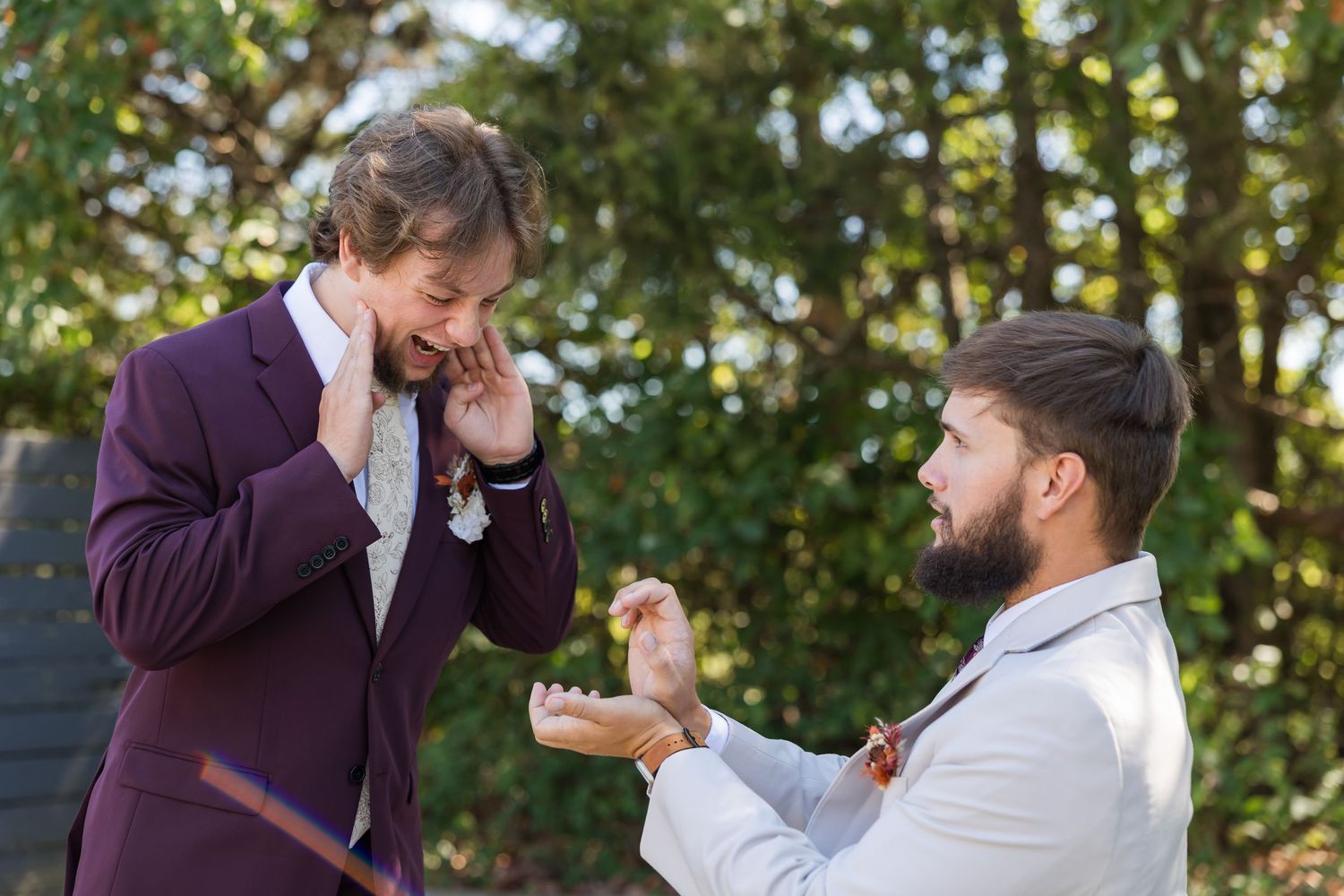 Two people share a joyful moment while standing outdoors with trees in the background.