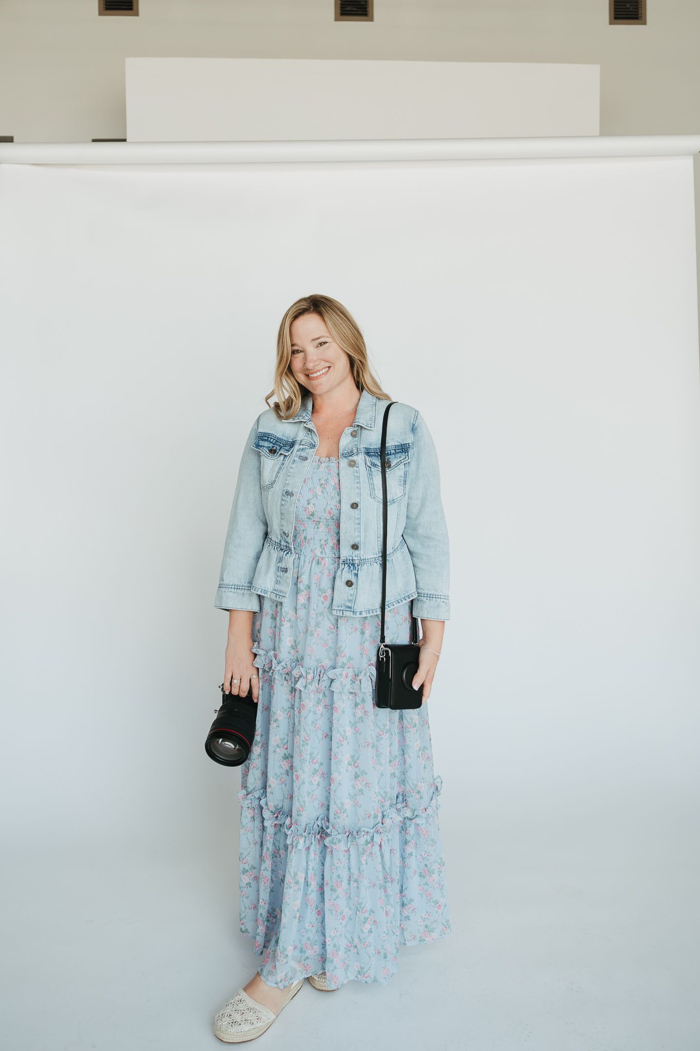 Casual spring outfit featuring light blue denim jacket paired with flowing floral maxi dress and comfortable sneakers.
