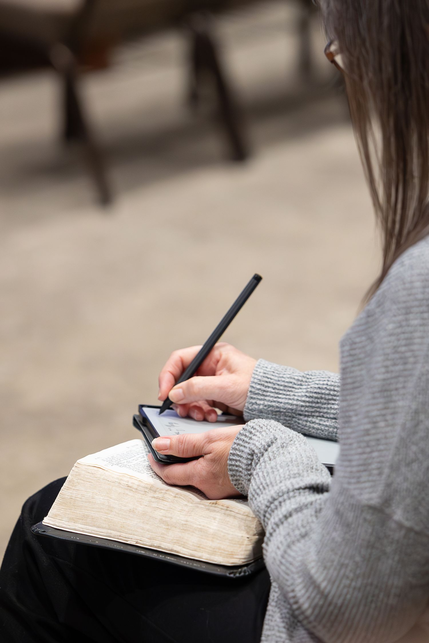 Close-up of hands writing notes in a book while wearing a gray sweater.