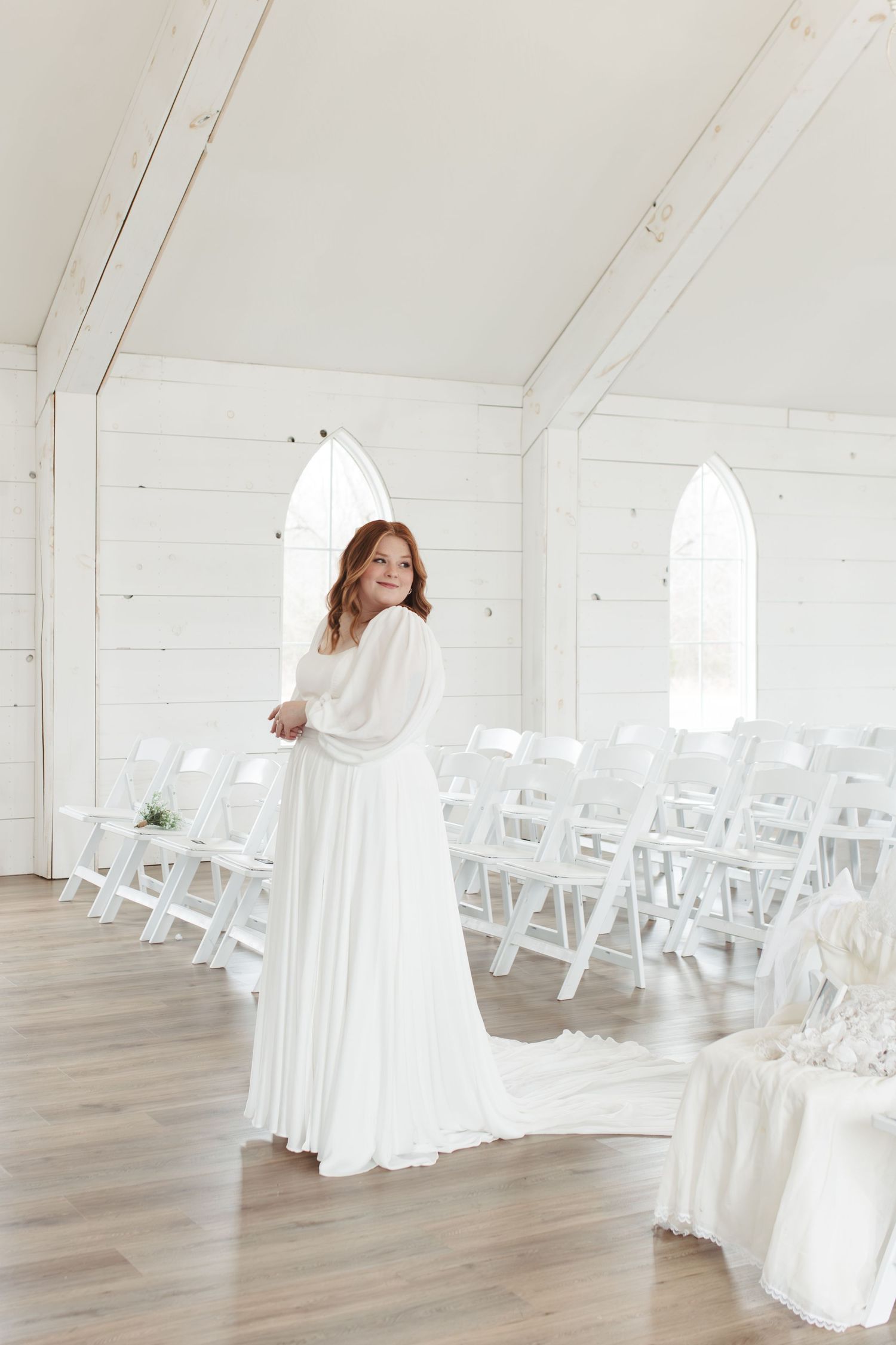 White chapel interior with rows of folding chairs and flowing wedding gown.