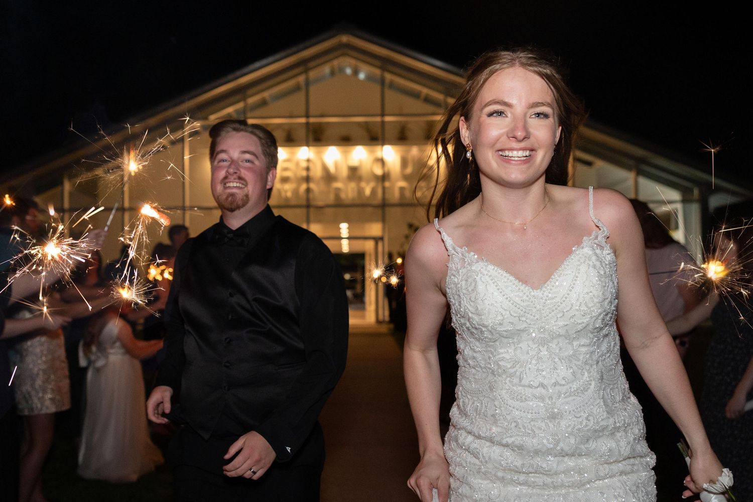 Wedding celebration at night with sparklers outside an illuminated venue.