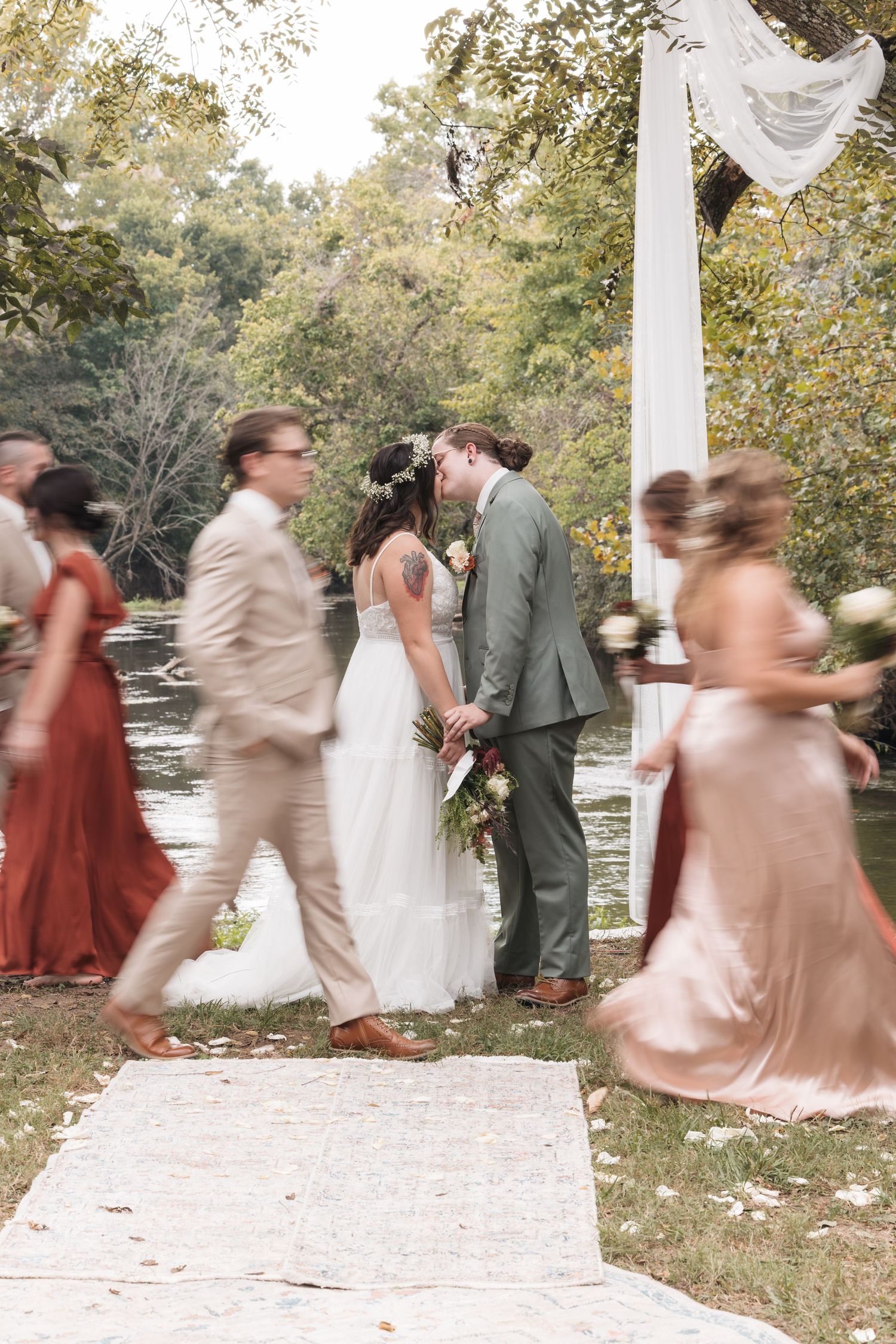Candid moment during outdoor wedding ceremony with white fabric arch and guests in neutral and rust tones.