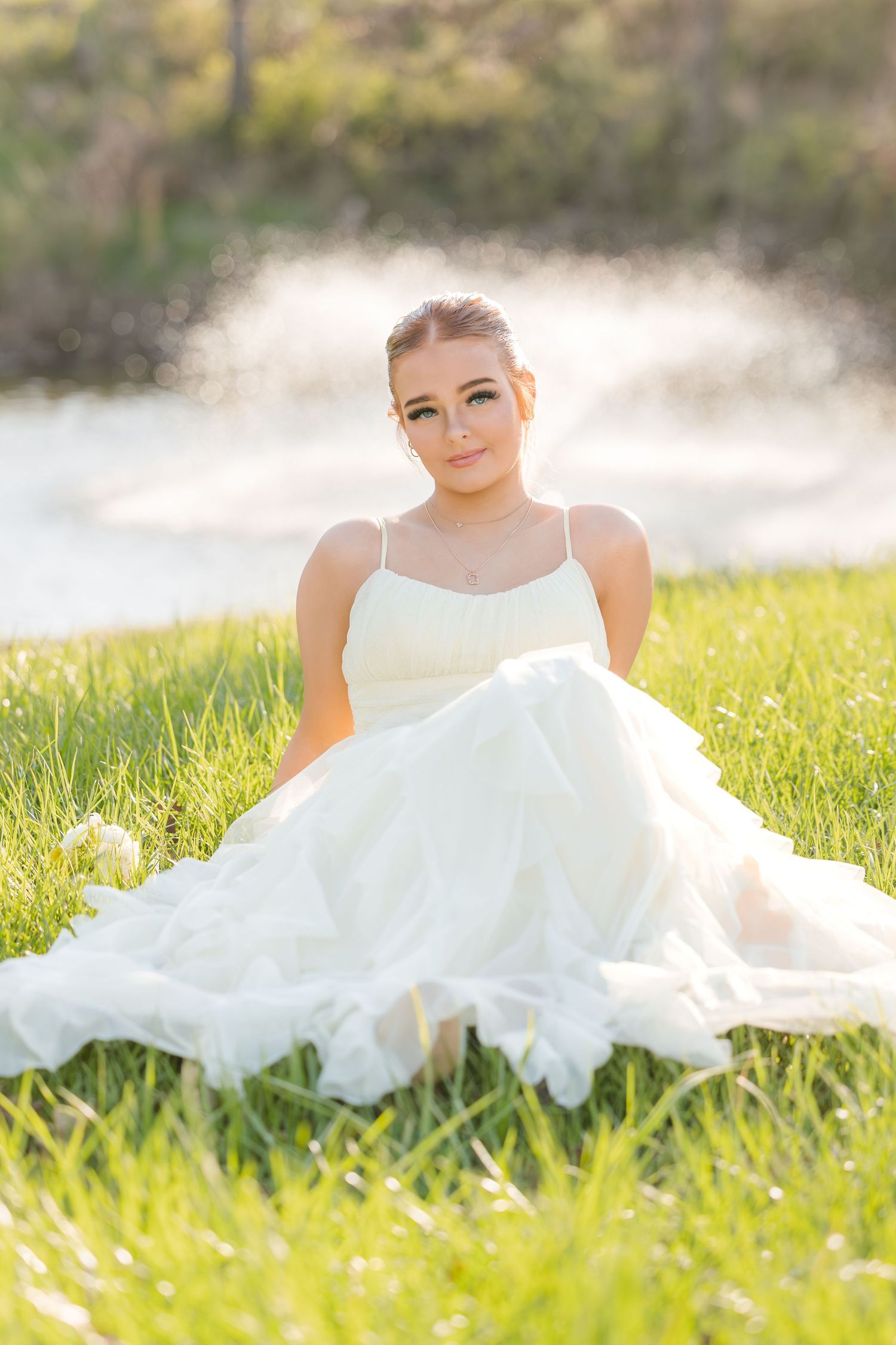 A white wedding dress flows across green grass in a sunlit outdoor setting with dreamy bokeh effect in background.