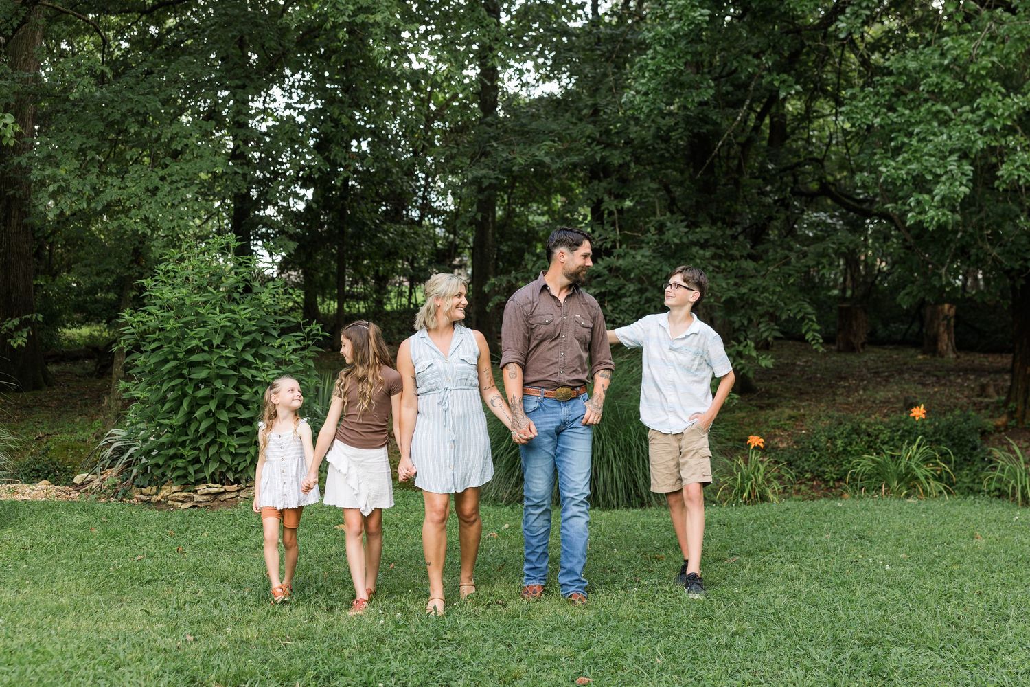 A family walks together on green grass with a wooded background on a summer day.