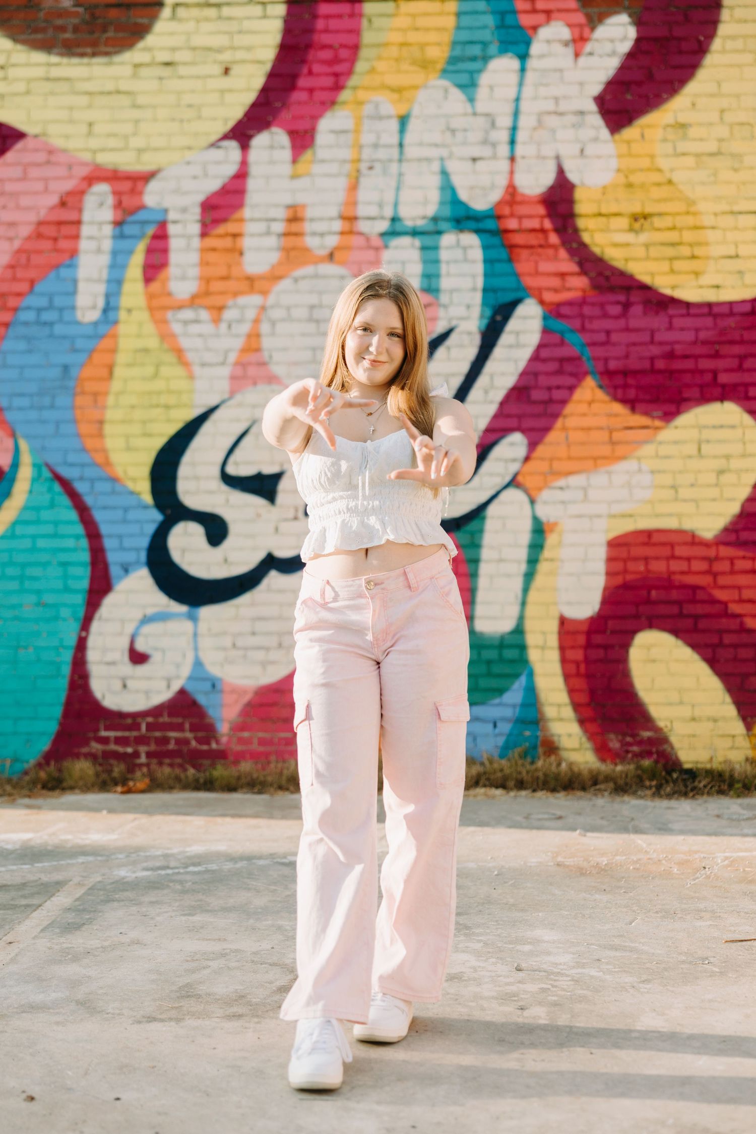 A person in pale pink loungewear strikes playful poses against a vibrant graffiti mural wall.