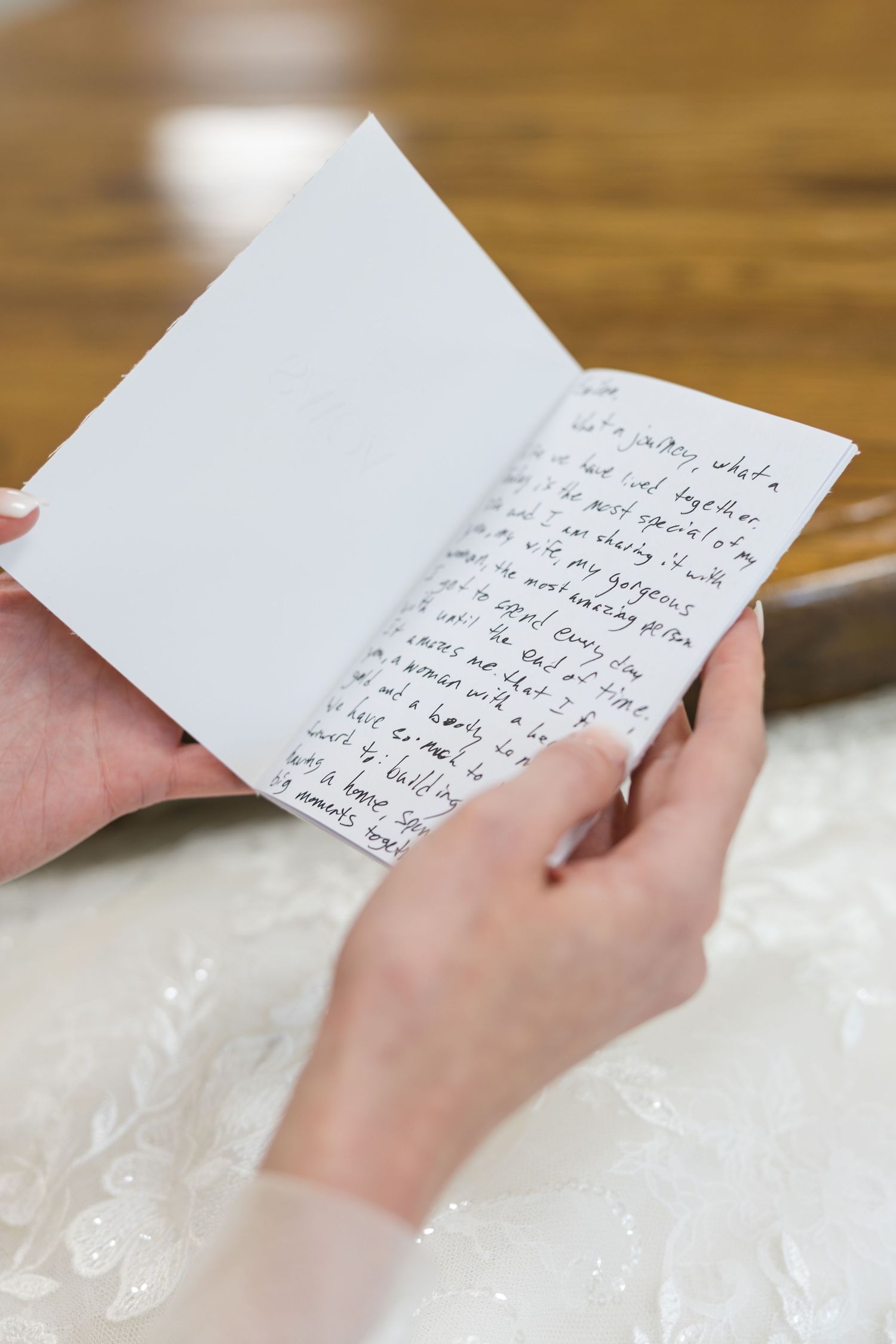 Bride reads handwritten letter from groom on wedding day while wearing white lace wedding dress.