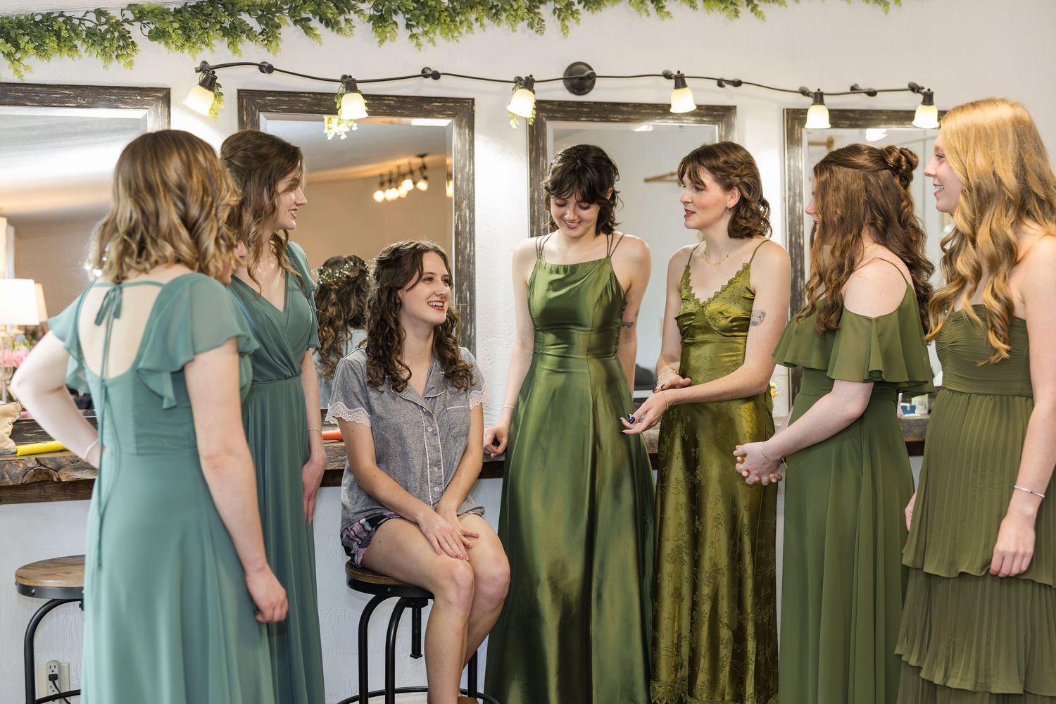Bridesmaids in green dresses chatting in bridal suite before wedding ceremony.