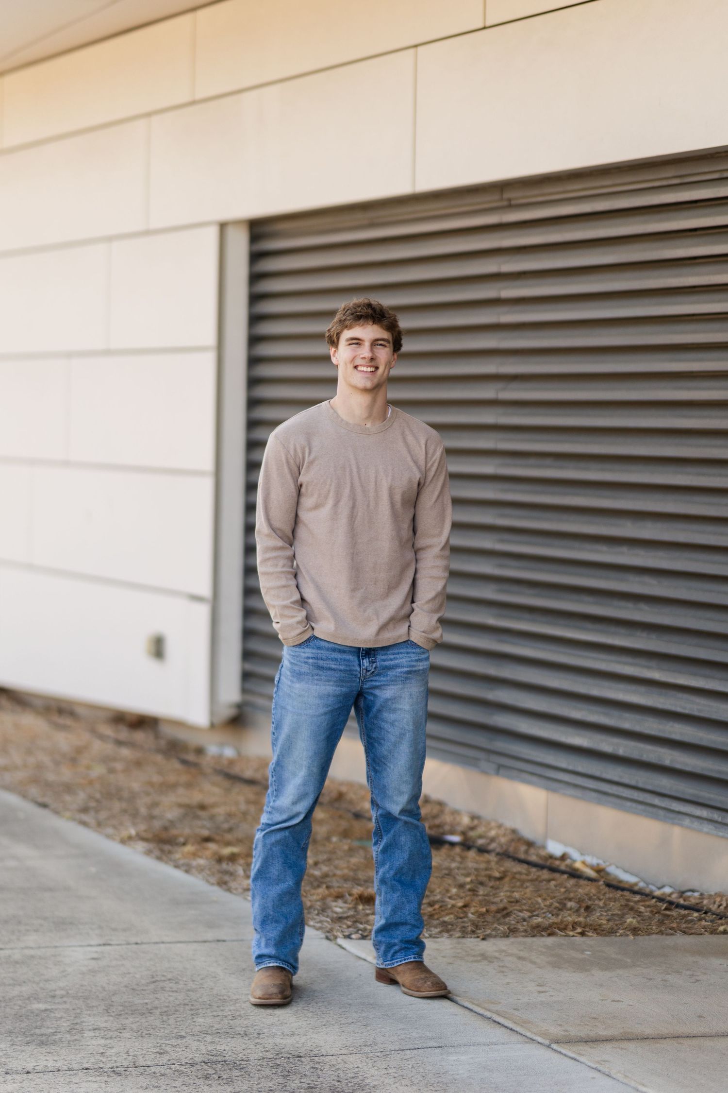Portrait of person in beige sweater and jeans standing against industrial wall.