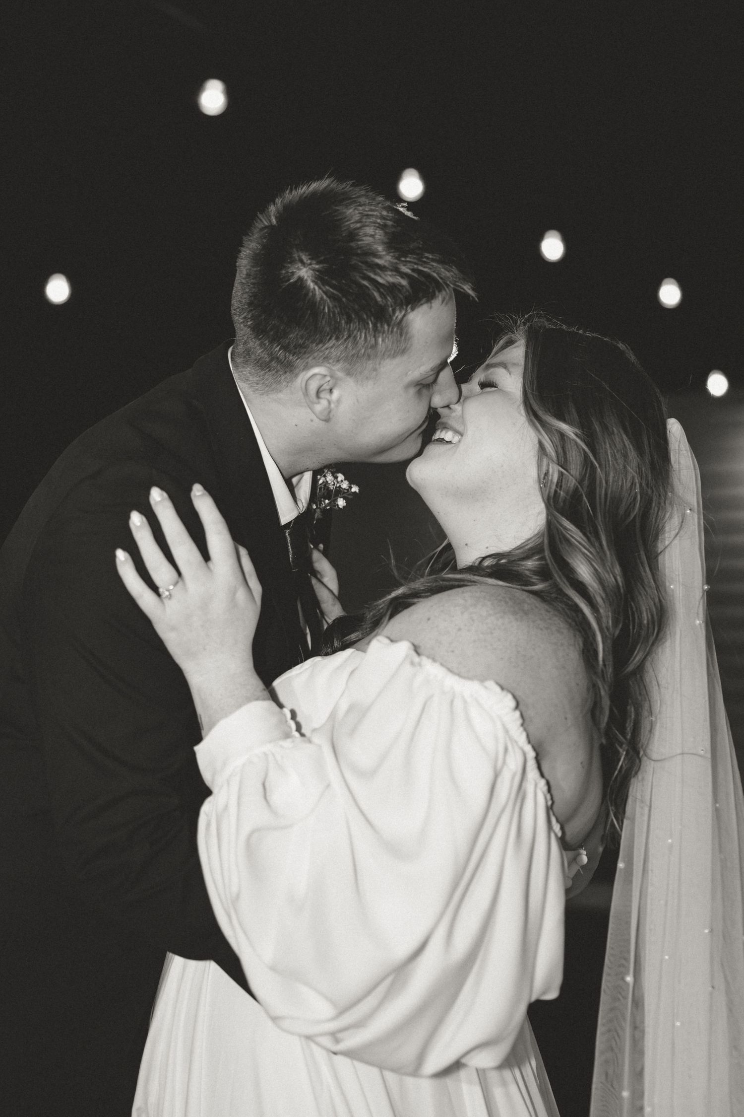 Romantic black and white portrait of couple sharing intimate moment under twinkle lights.