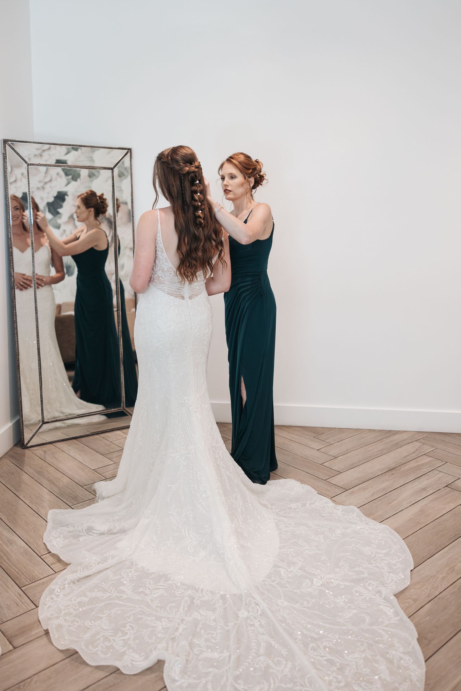 Long lace wedding dress with dramatic train being adjusted in front of mirror.