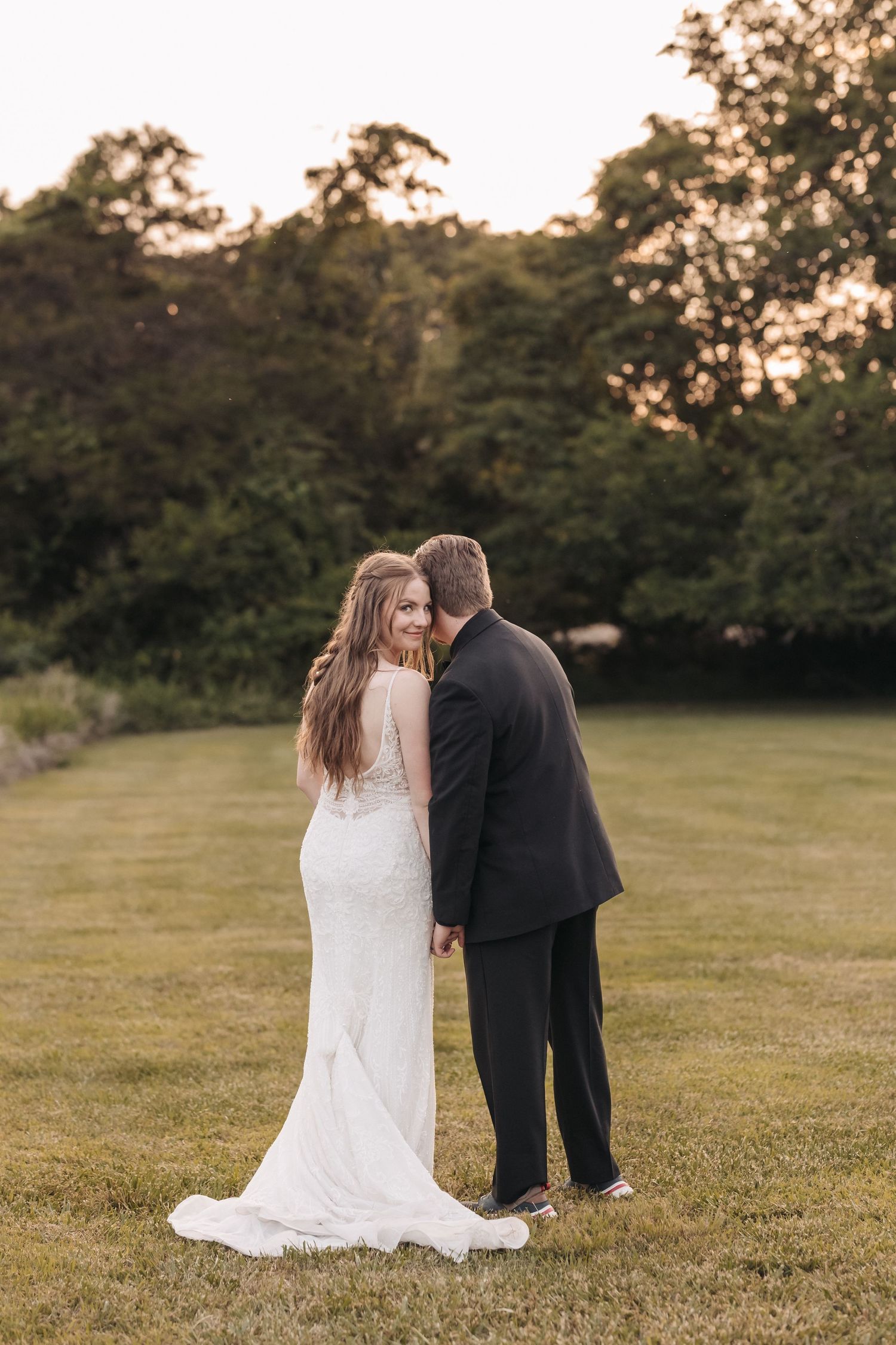 A tender moment between newlyweds standing in a serene outdoor setting at sunset.
