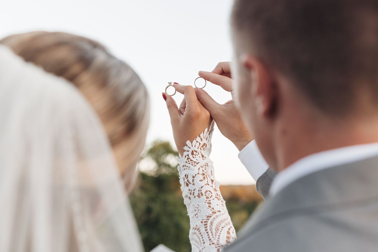 Close-up of hands exchanging ring during outdoor wedding ceremony.