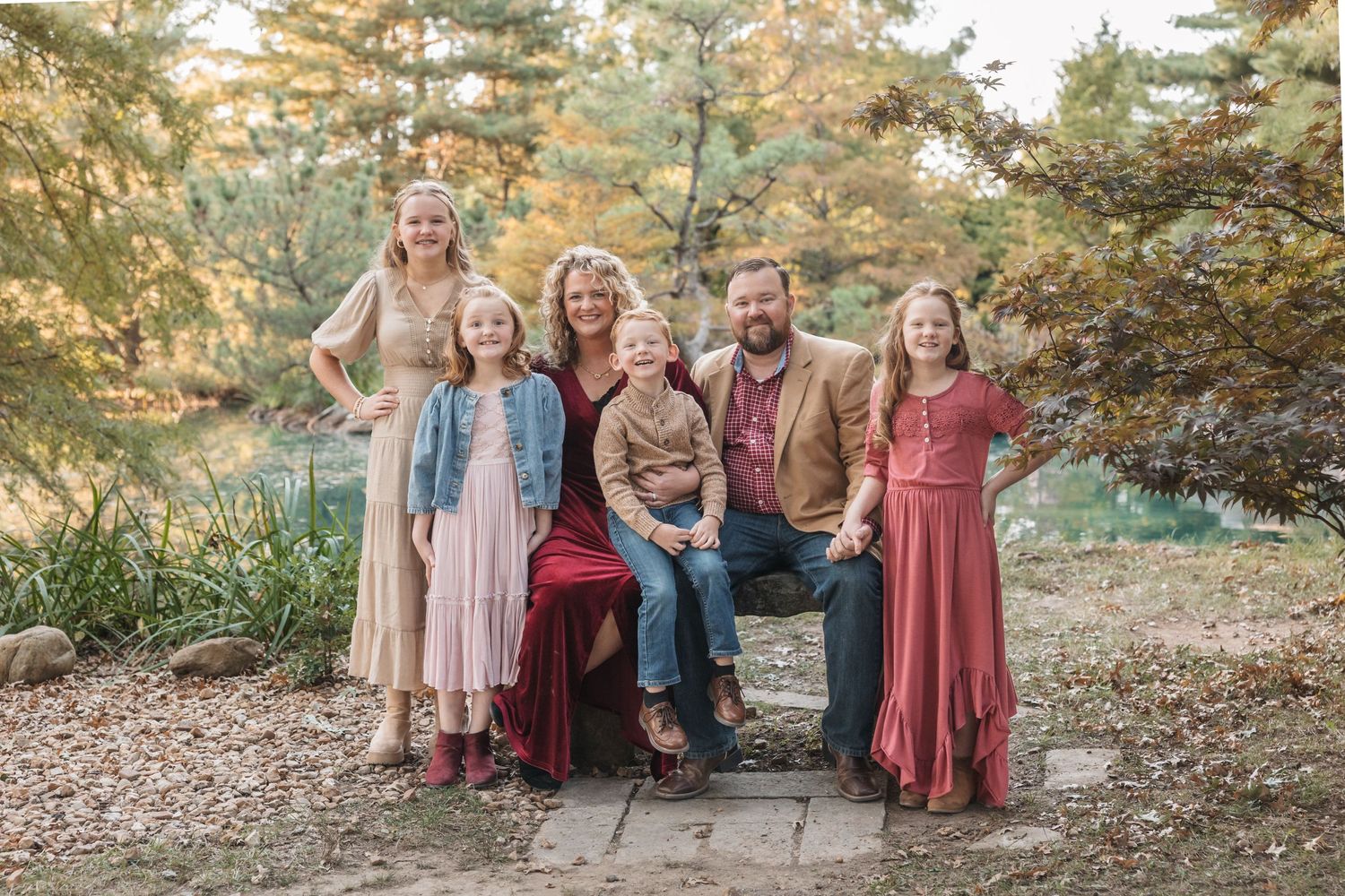 Family sitting together on stone steps surrounded by autumn foliage.