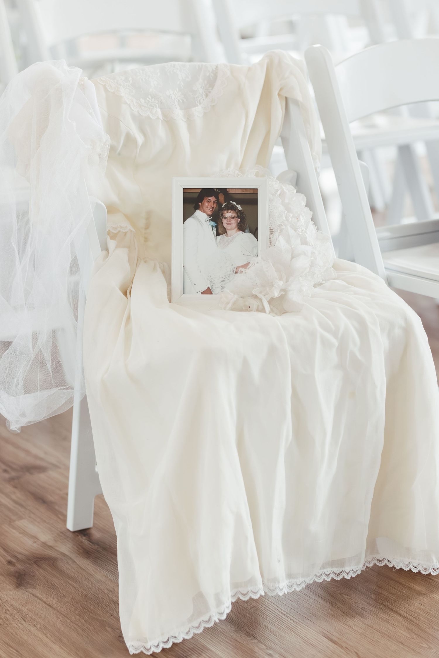 White lace wedding dress draped over chair with vintage photograph.