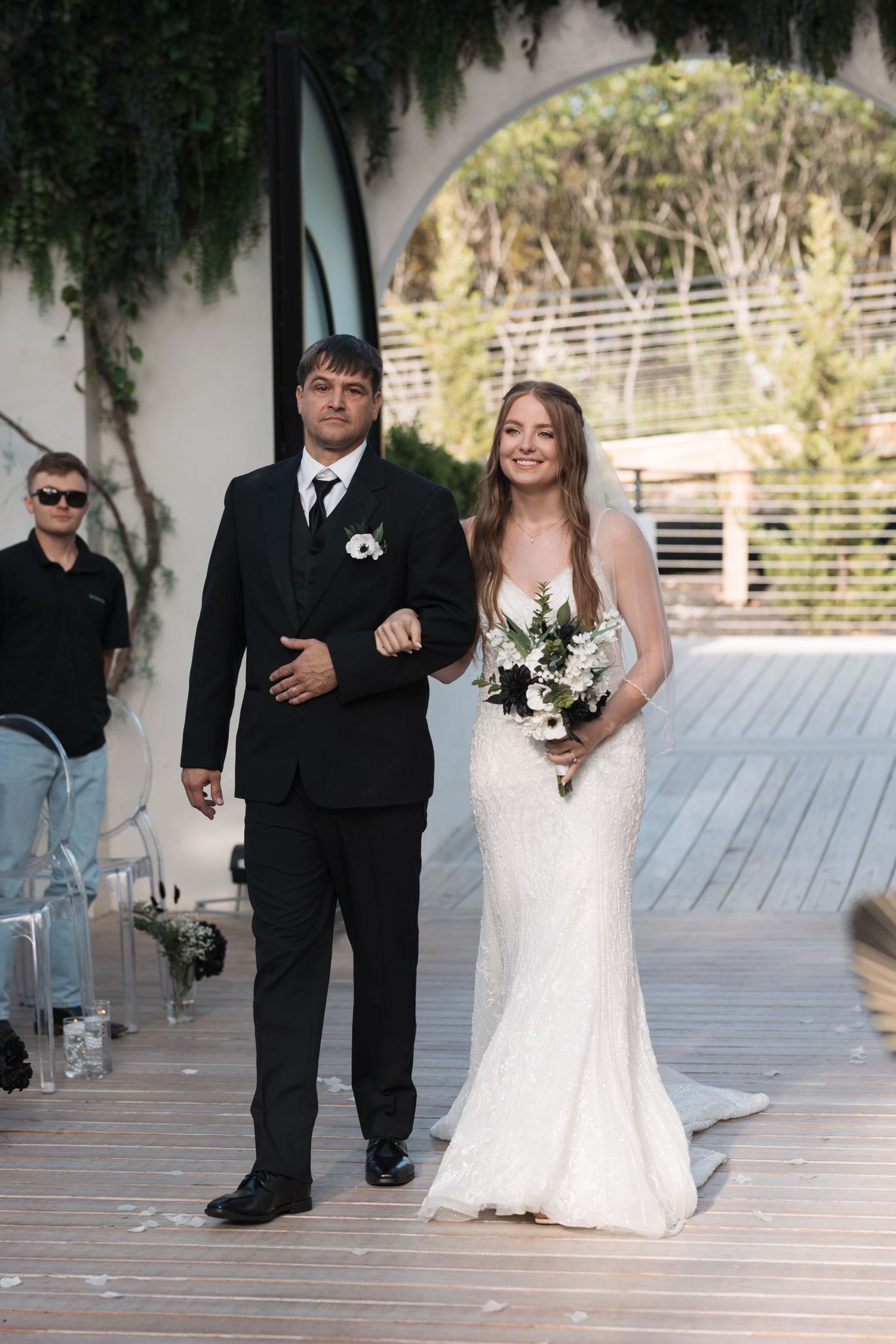 A couple walks down the aisle at an outdoor wedding ceremony with white decor.